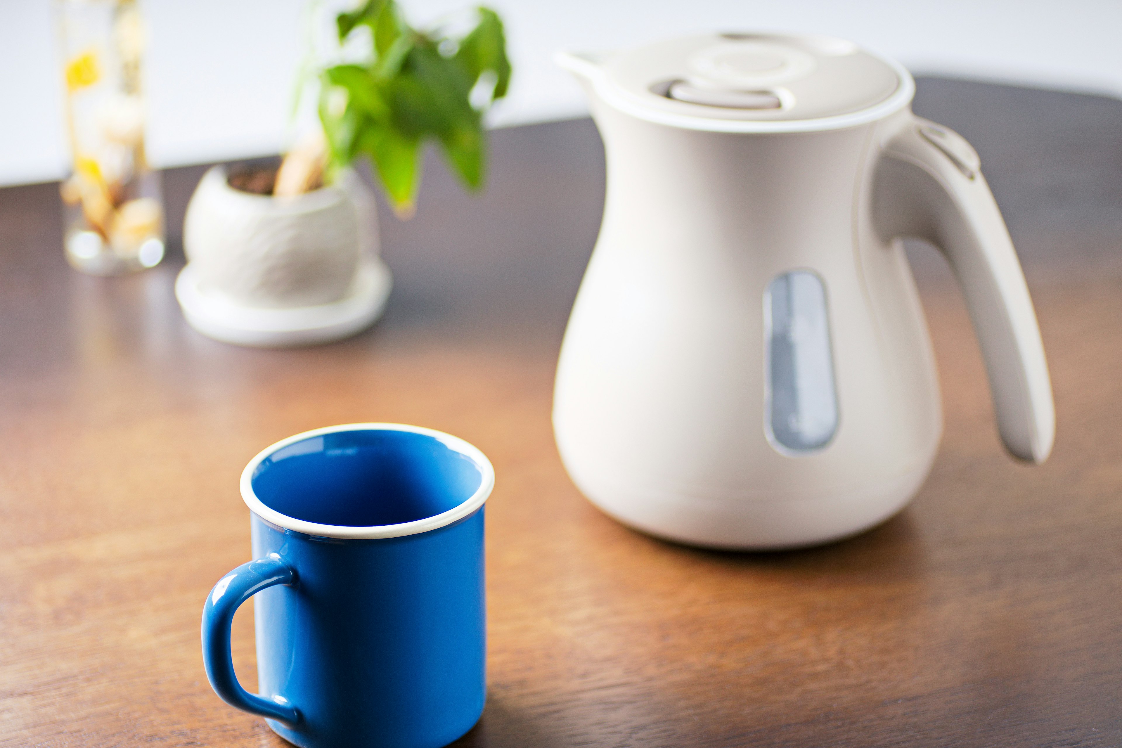 Ein weißer Wasserkocher und eine blaue Tasse auf einem Holztisch