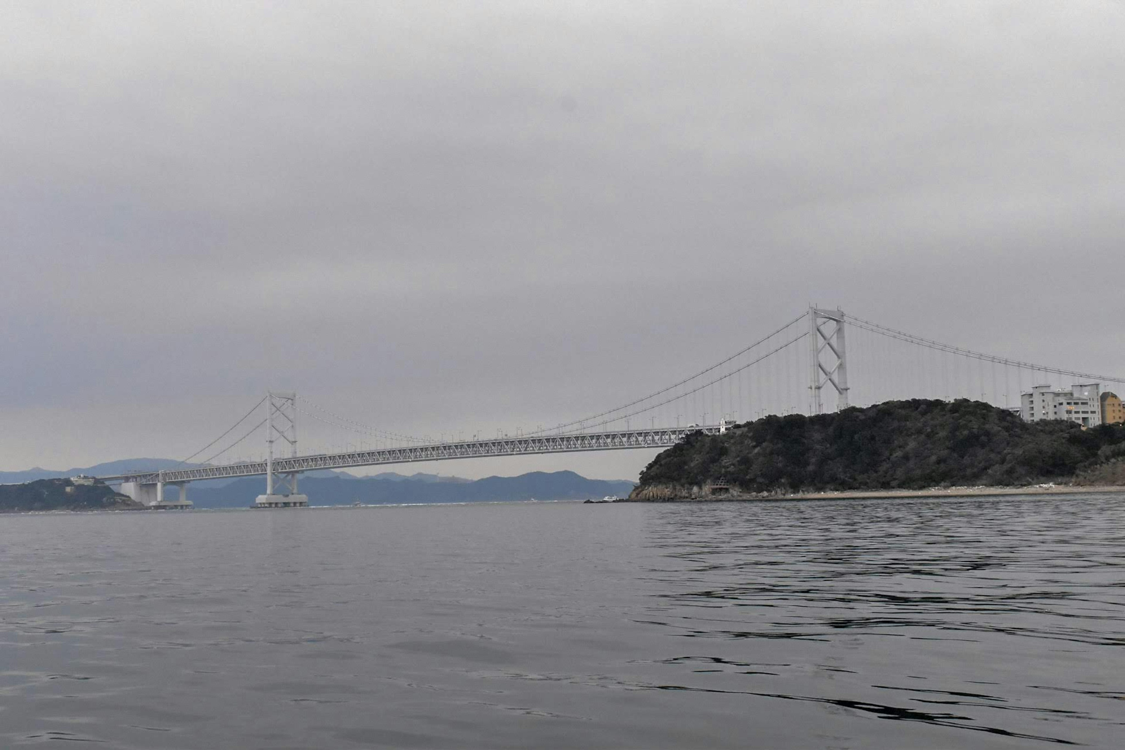 Vista escénica de un puente colgante sobre el agua con nubes grises y superficie tranquila