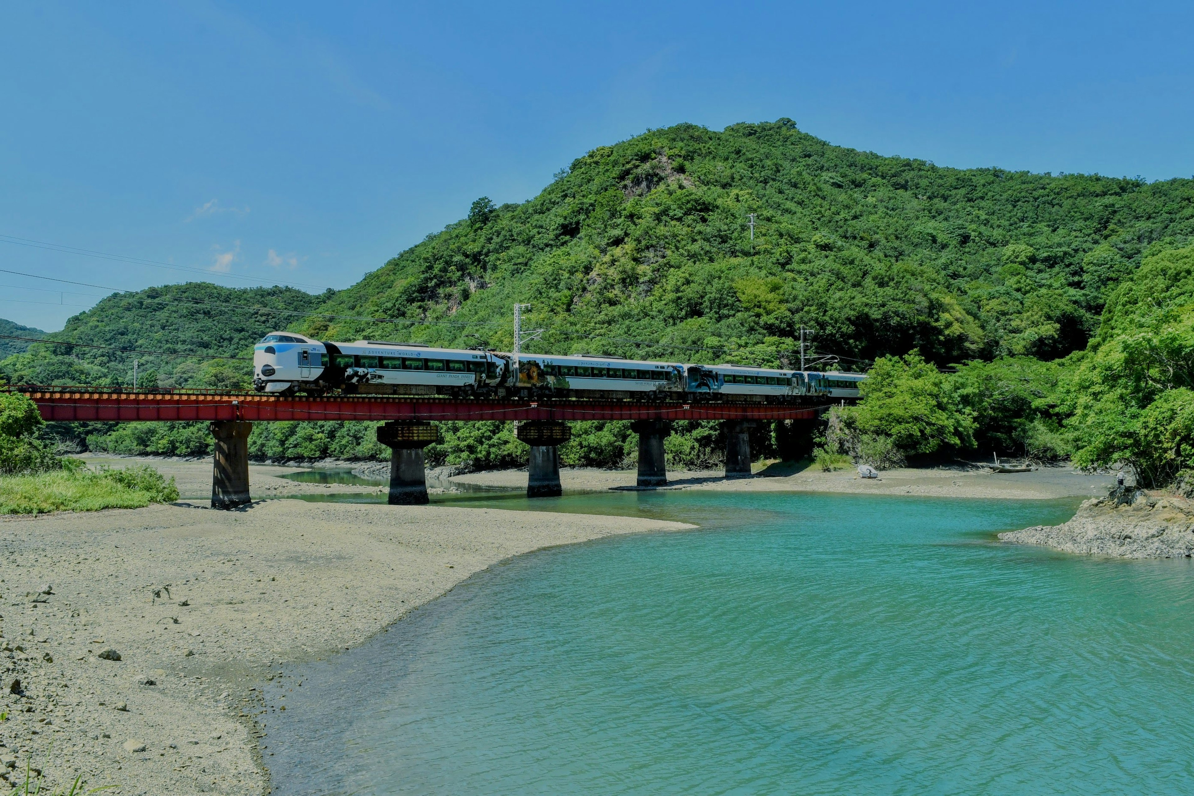 一列火車穿過橋樑，周圍是郁郁蔥蔥的山脈和河流