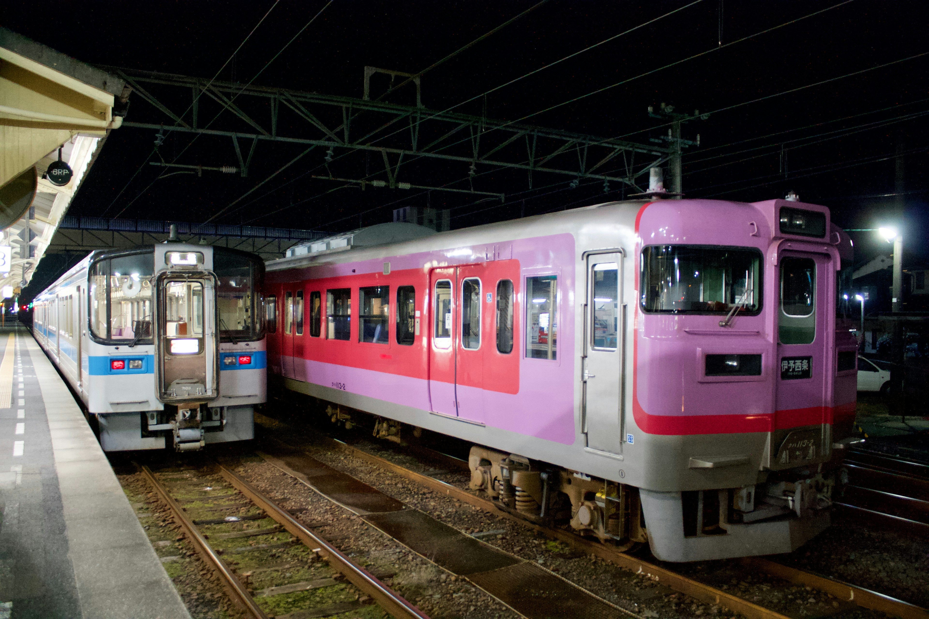 Dos trenes en una estación durante la noche uno rosa y uno gris