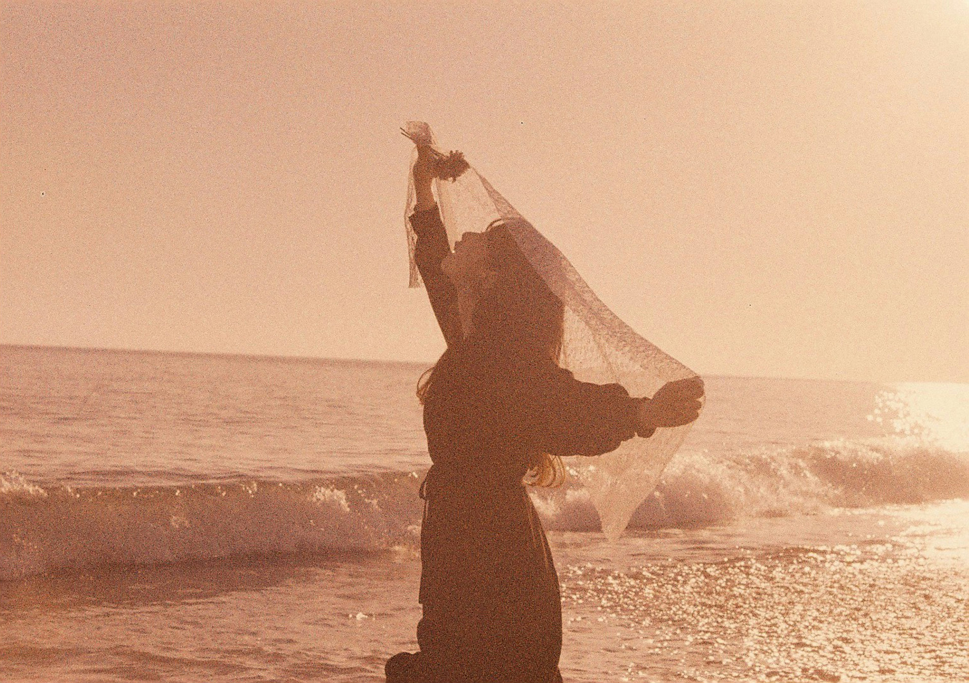 Mujer sosteniendo un pañuelo contra el atardecer en la playa