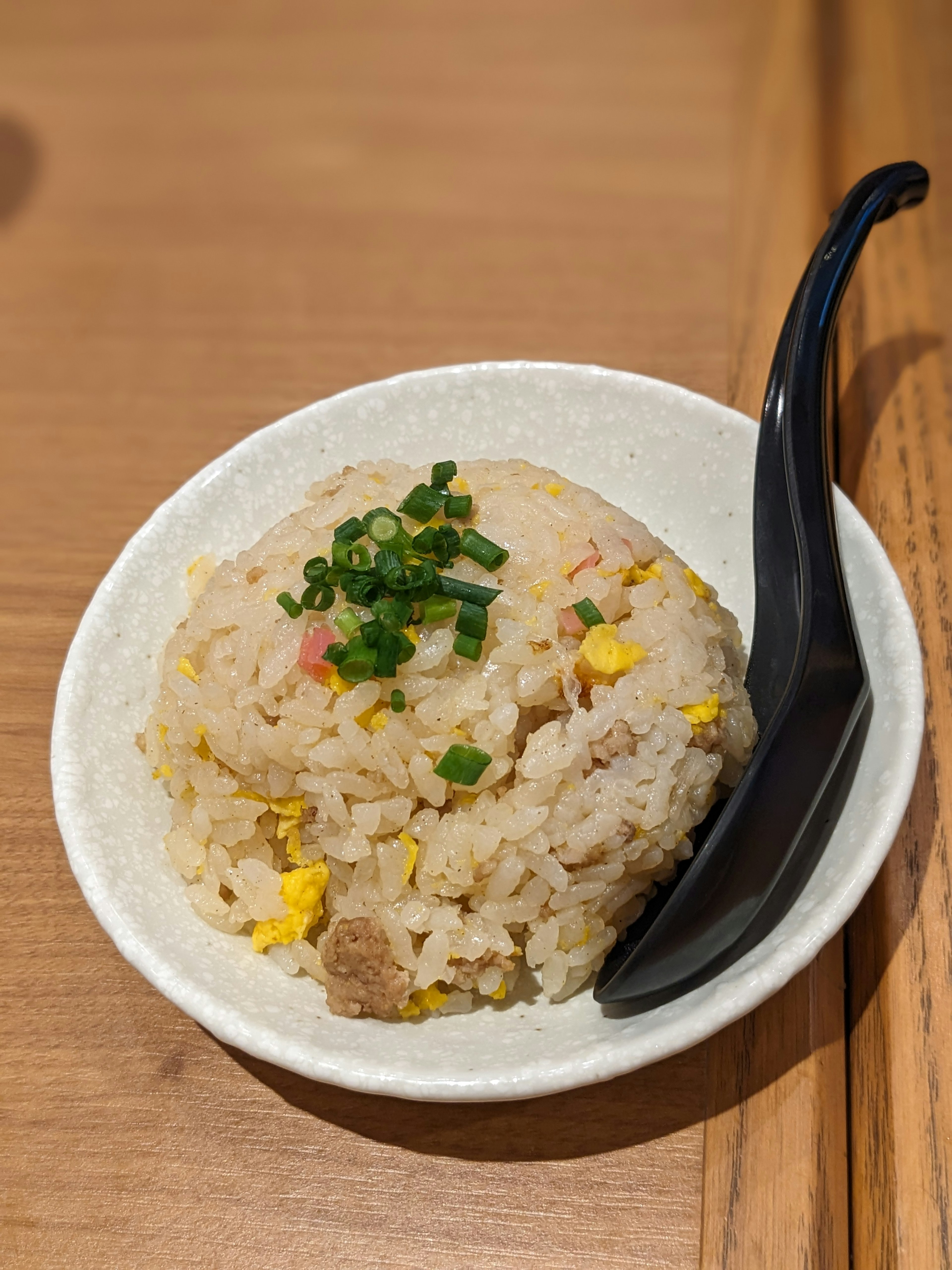 Arroz frito servido en un tazón blanco cubierto con cebollín picado