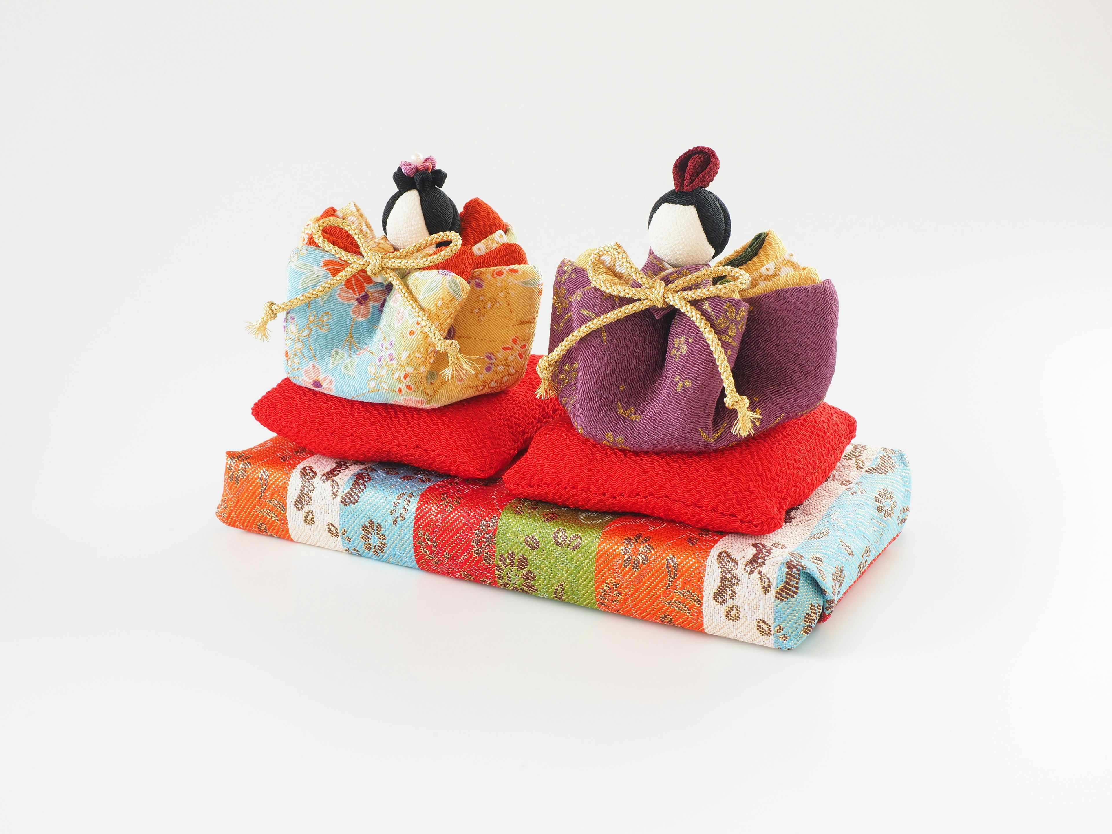 Traditional Japanese hina dolls sitting on colorful fabric cushions