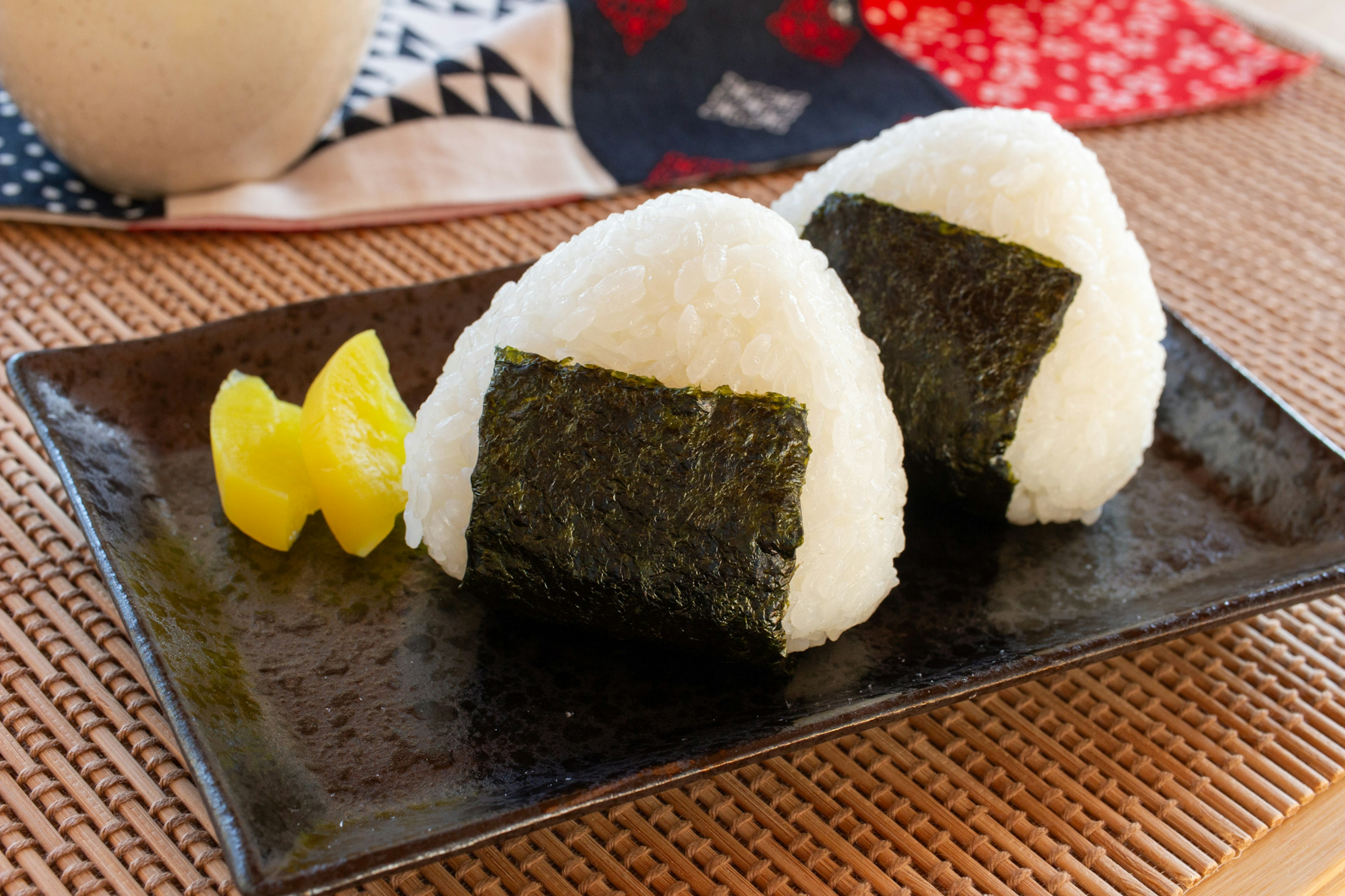 Two rice balls on a black plate with pickled ginger on the side