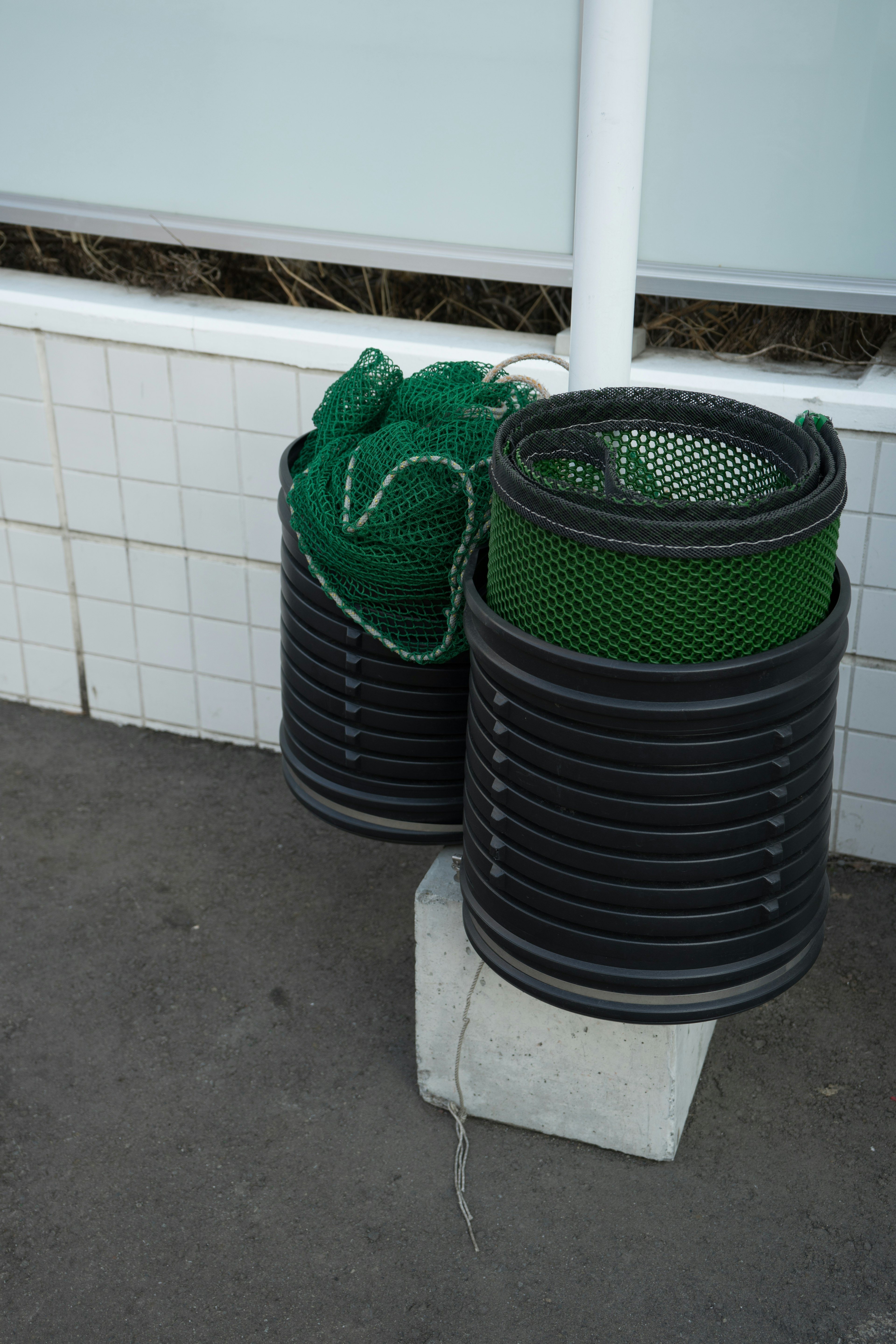 Stacked black trash bins with green netting