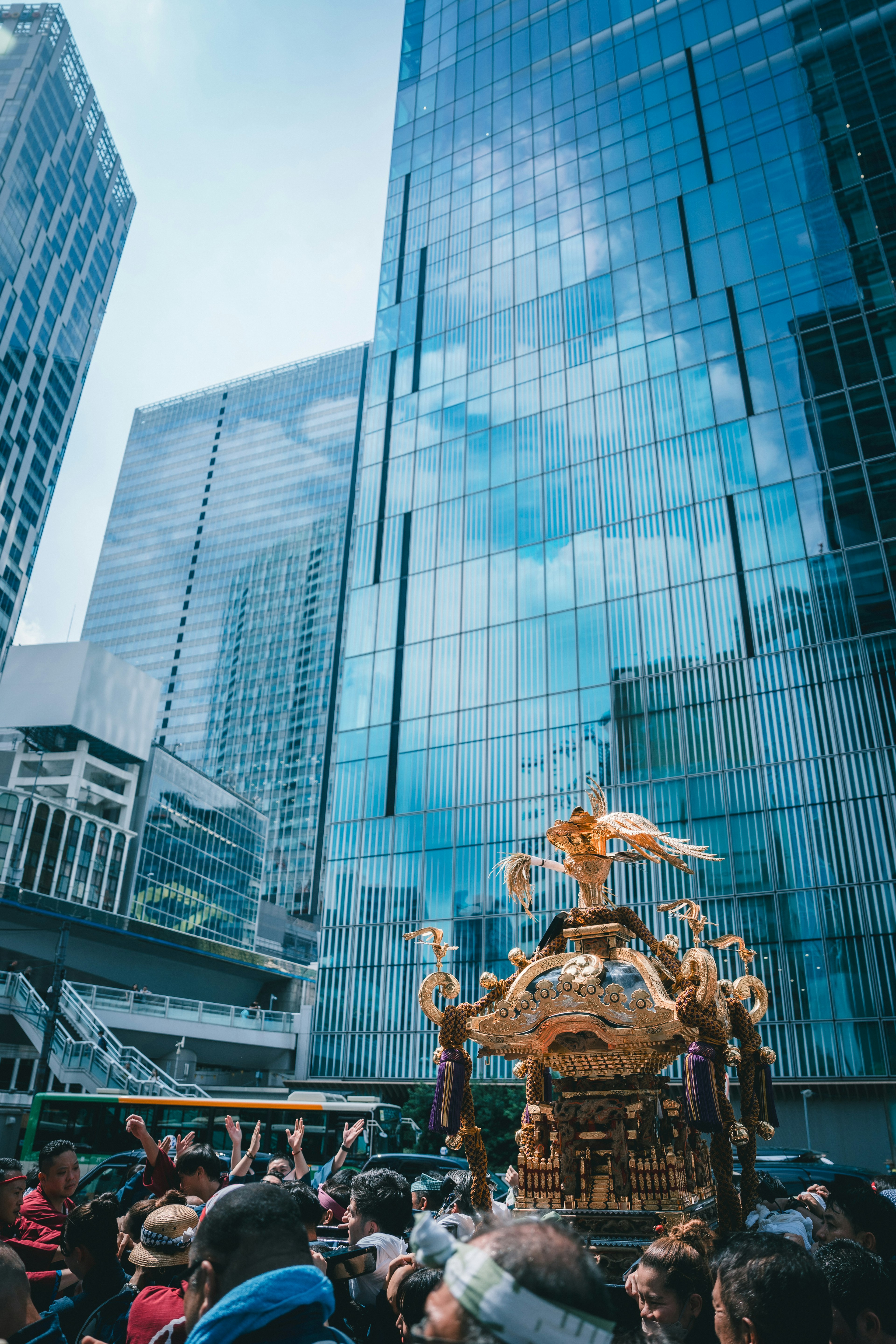 Crowd participating in a festival with a golden float amidst skyscrapers