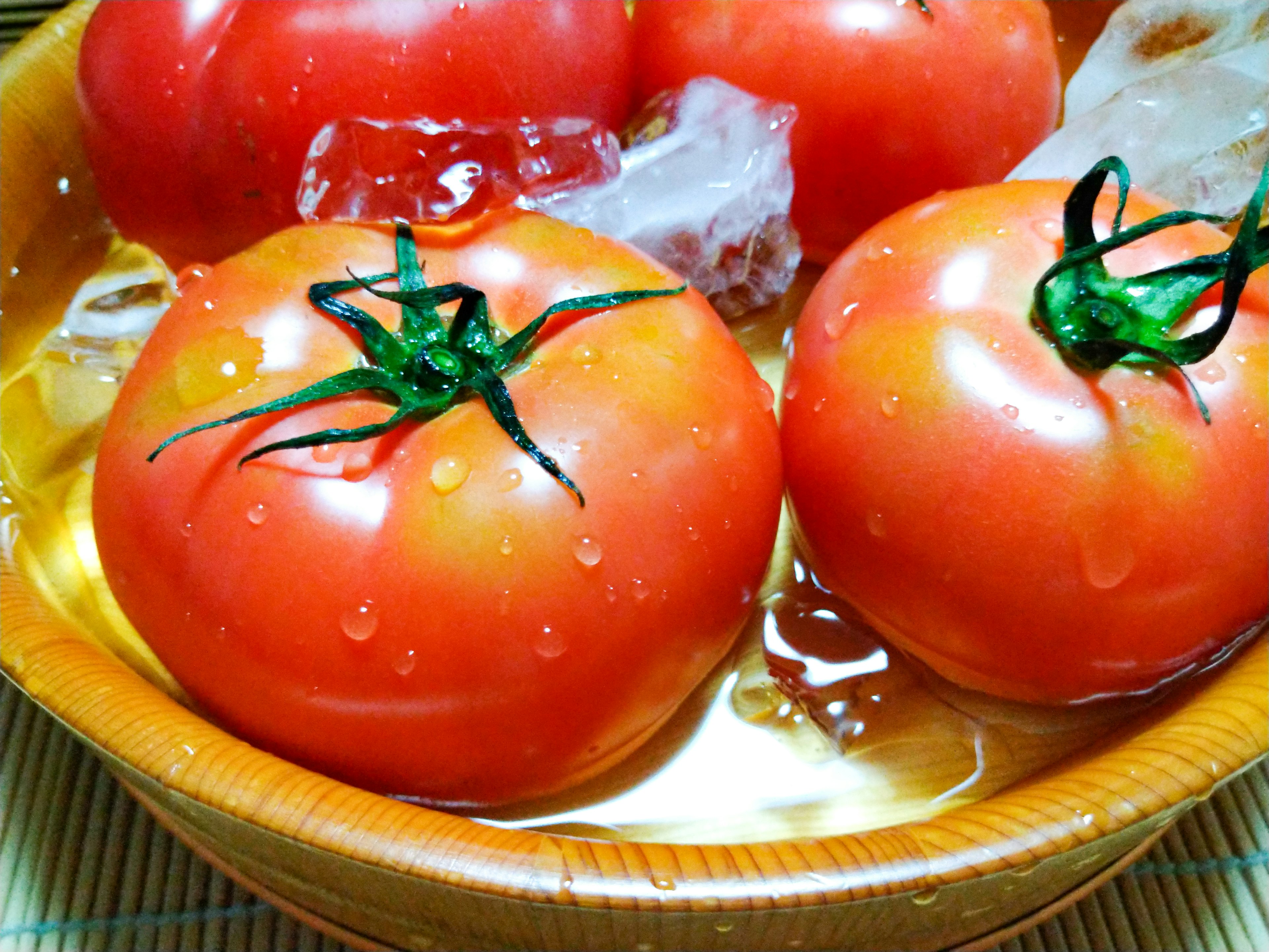 Tomates fraîches flottant dans de la glace et de l'eau dans un bol en bois