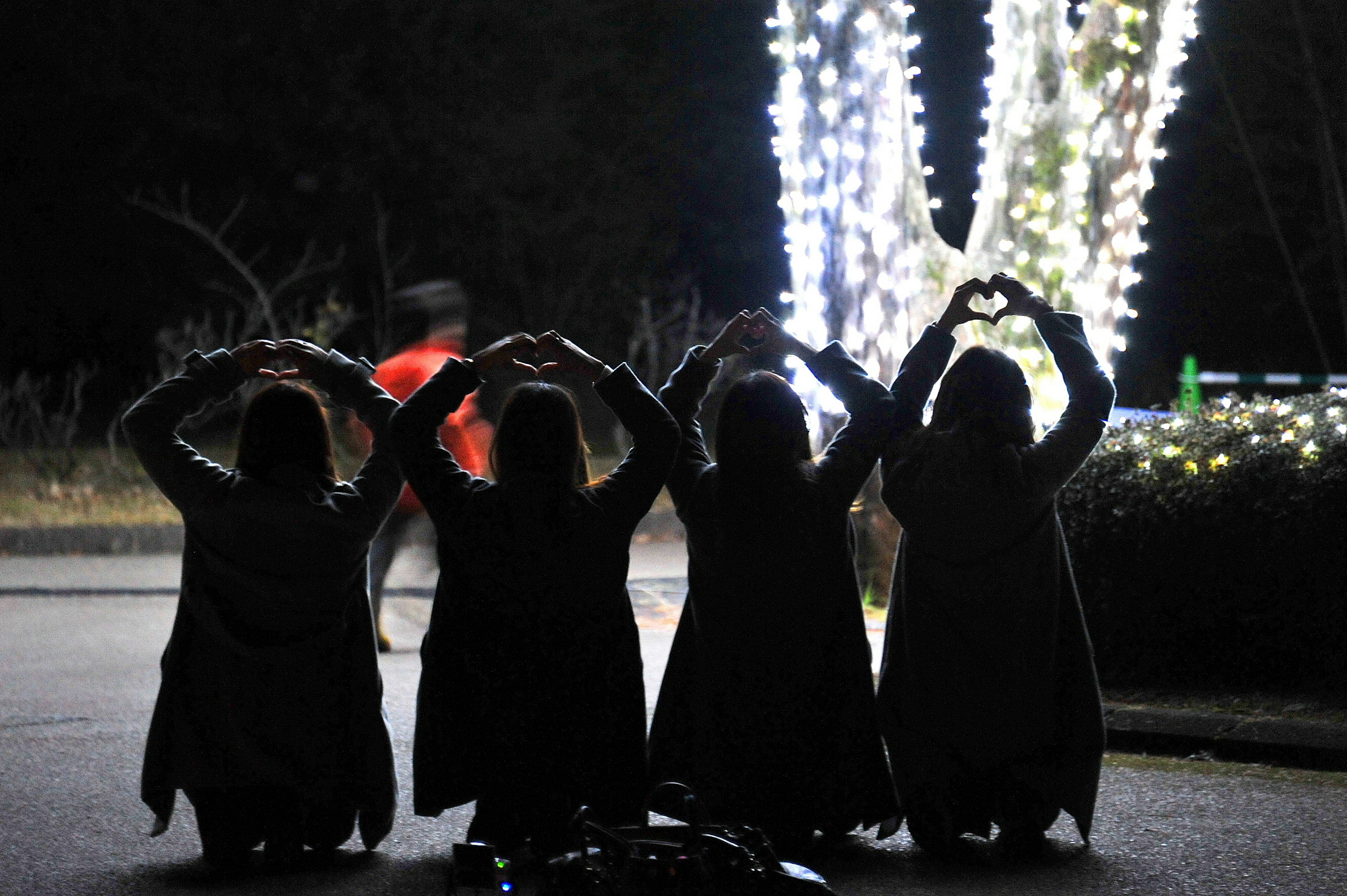 Cuatro mujeres formando corazones con las manos contra un fondo nocturno