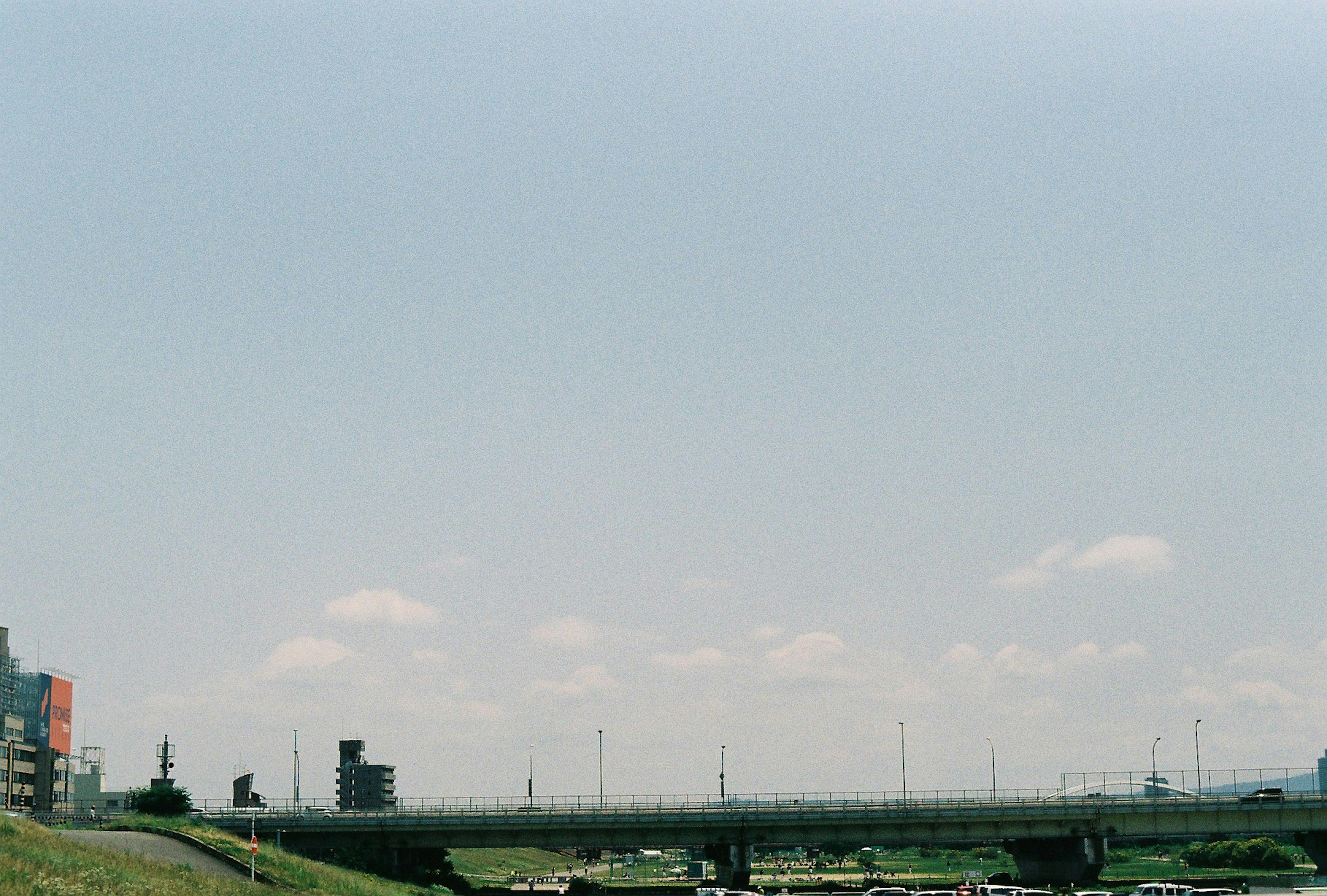 Landschaft mit blauem Himmel und Wolken entlang eines Flusses und einer Brücke