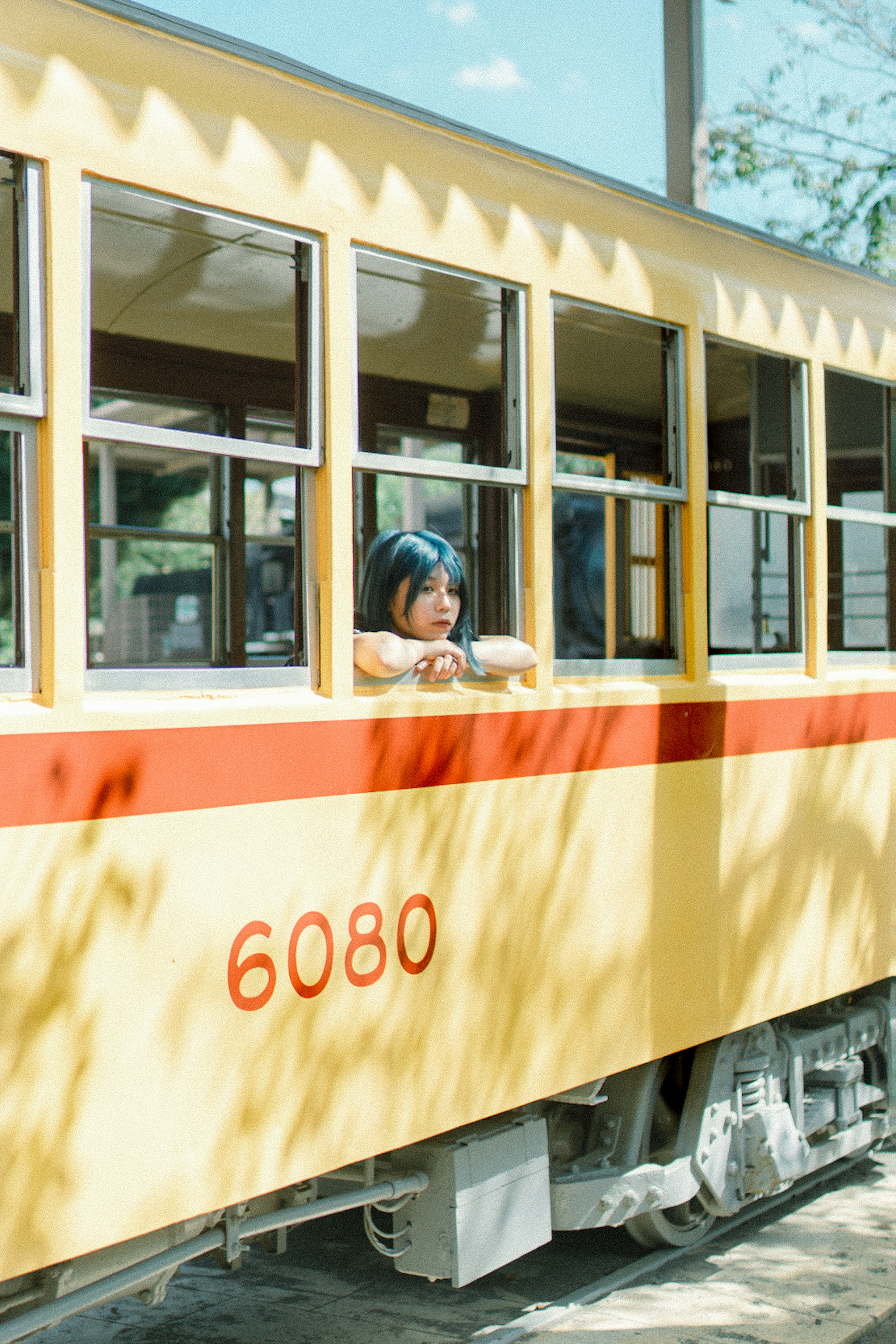 Una chica con cabello azul mirando por la ventana de un tren amarillo