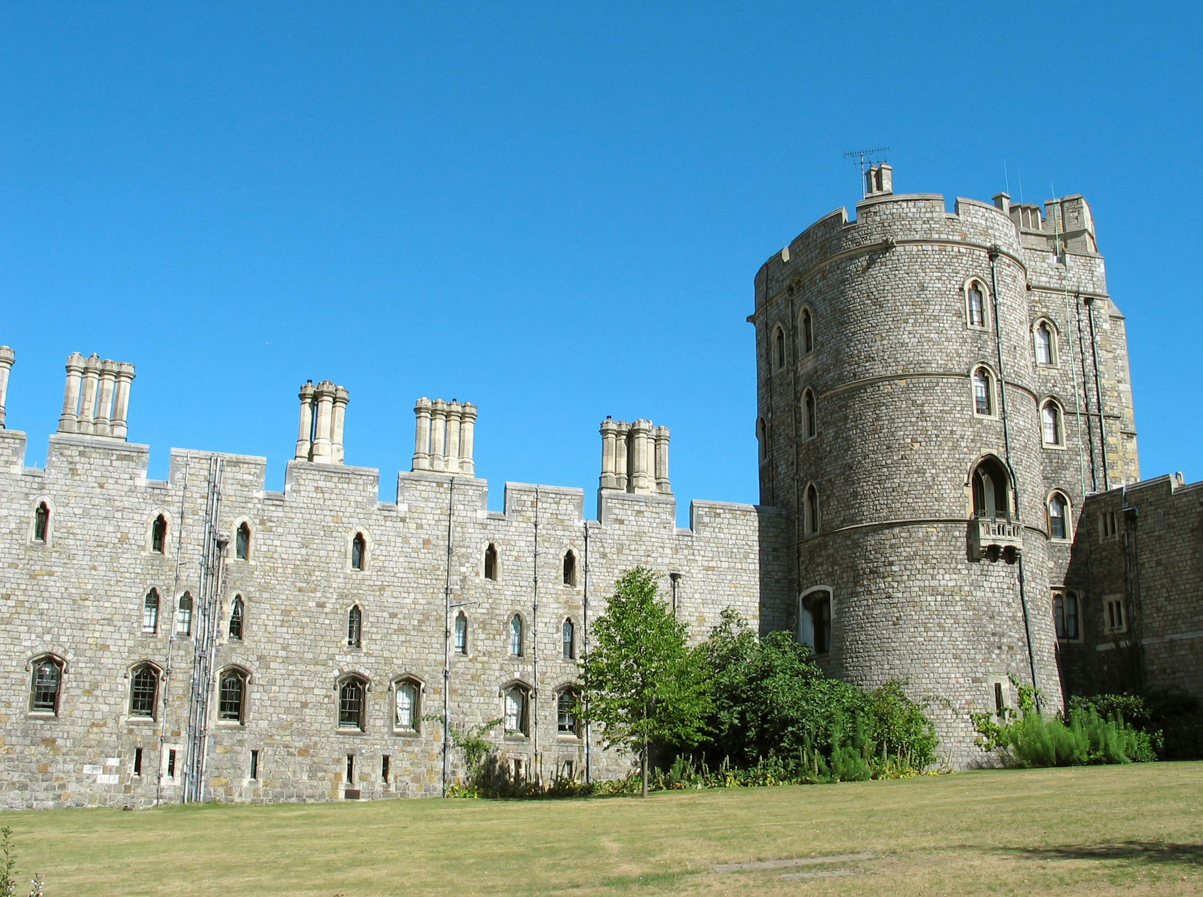 Stone castle walls and tower under blue sky with green grass