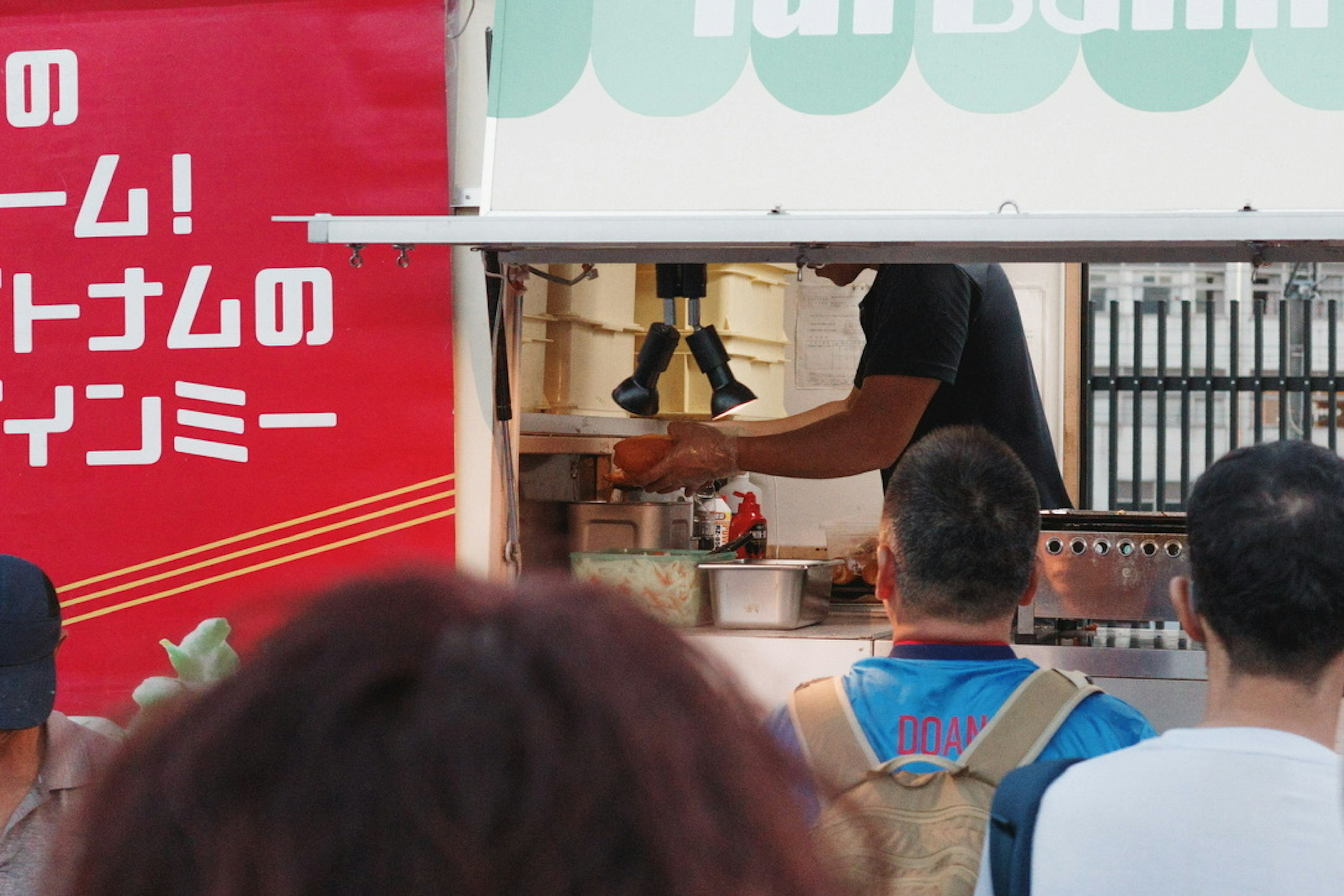 Koch, der Essen in einem Foodtruck zubereitet, mit Menschen in der Warteschlange