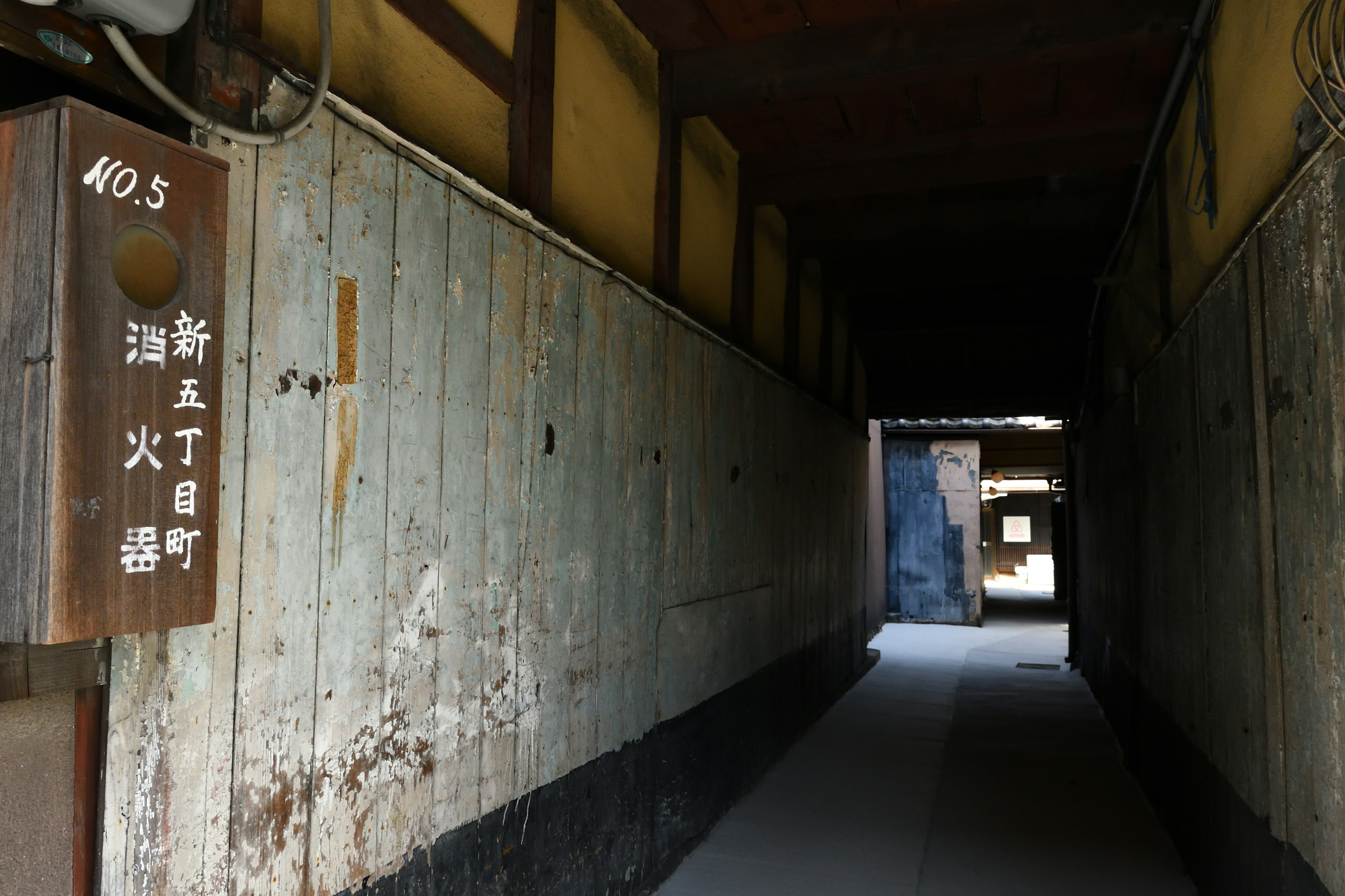 Narrow corridor of an old Japanese street with weathered wooden walls a sign displaying a number and name