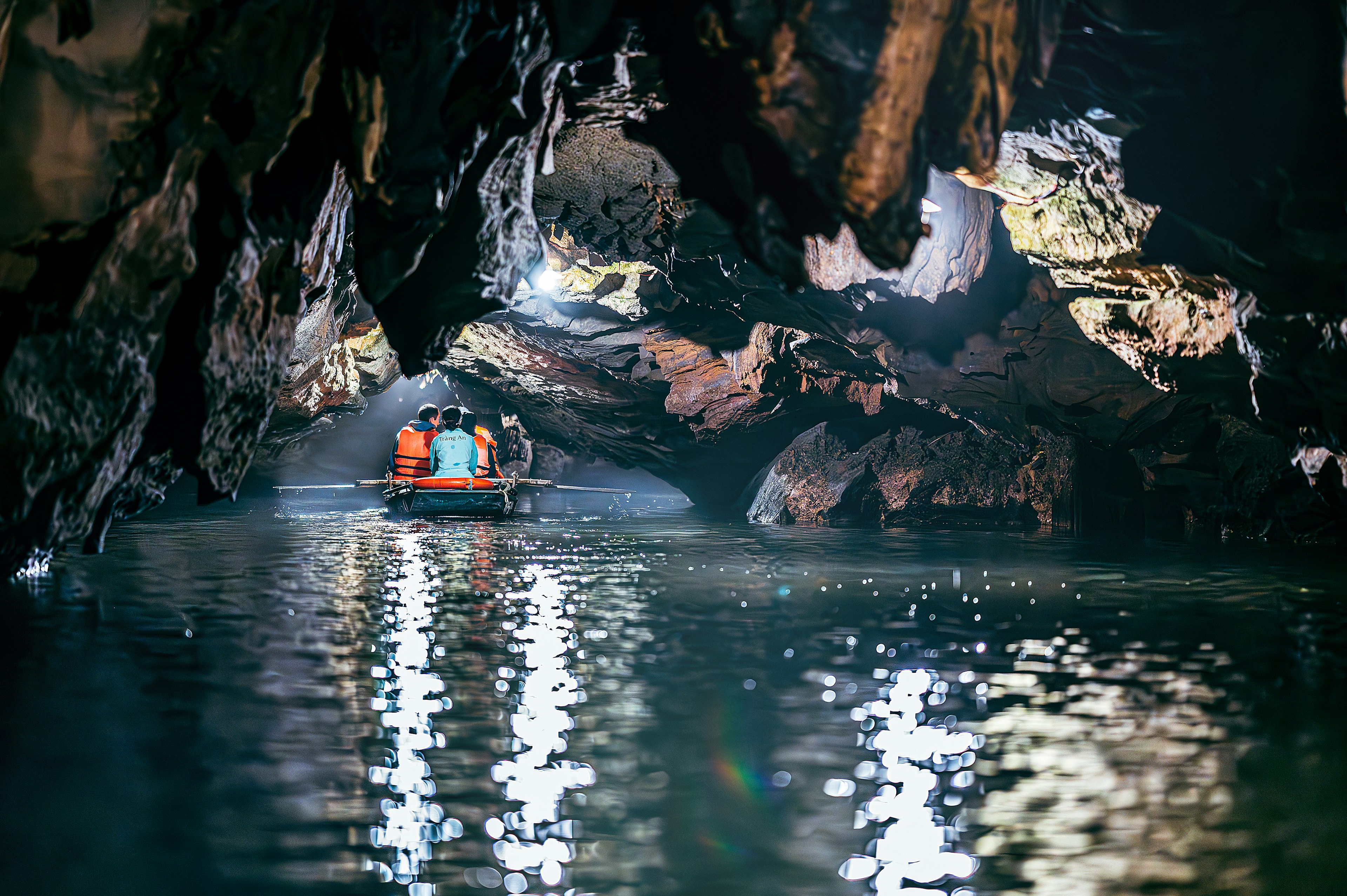 Menschen in einem Boot in einer dunklen Höhle mit Reflexionen auf der Wasseroberfläche