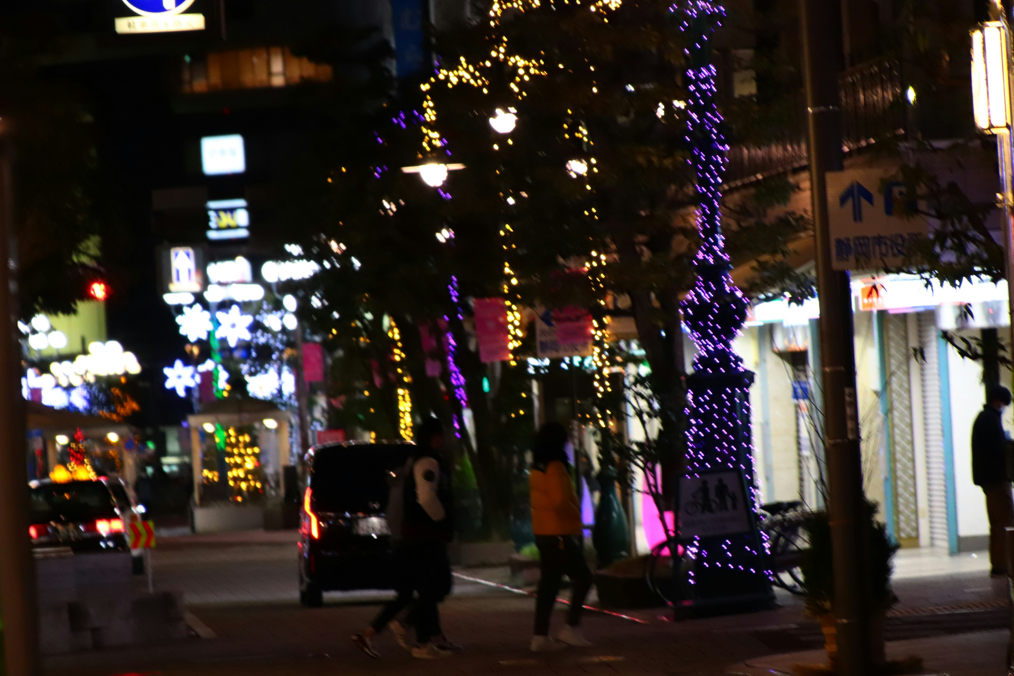 Scène de rue nocturne colorée avec des arbres illuminés et des gens marchant