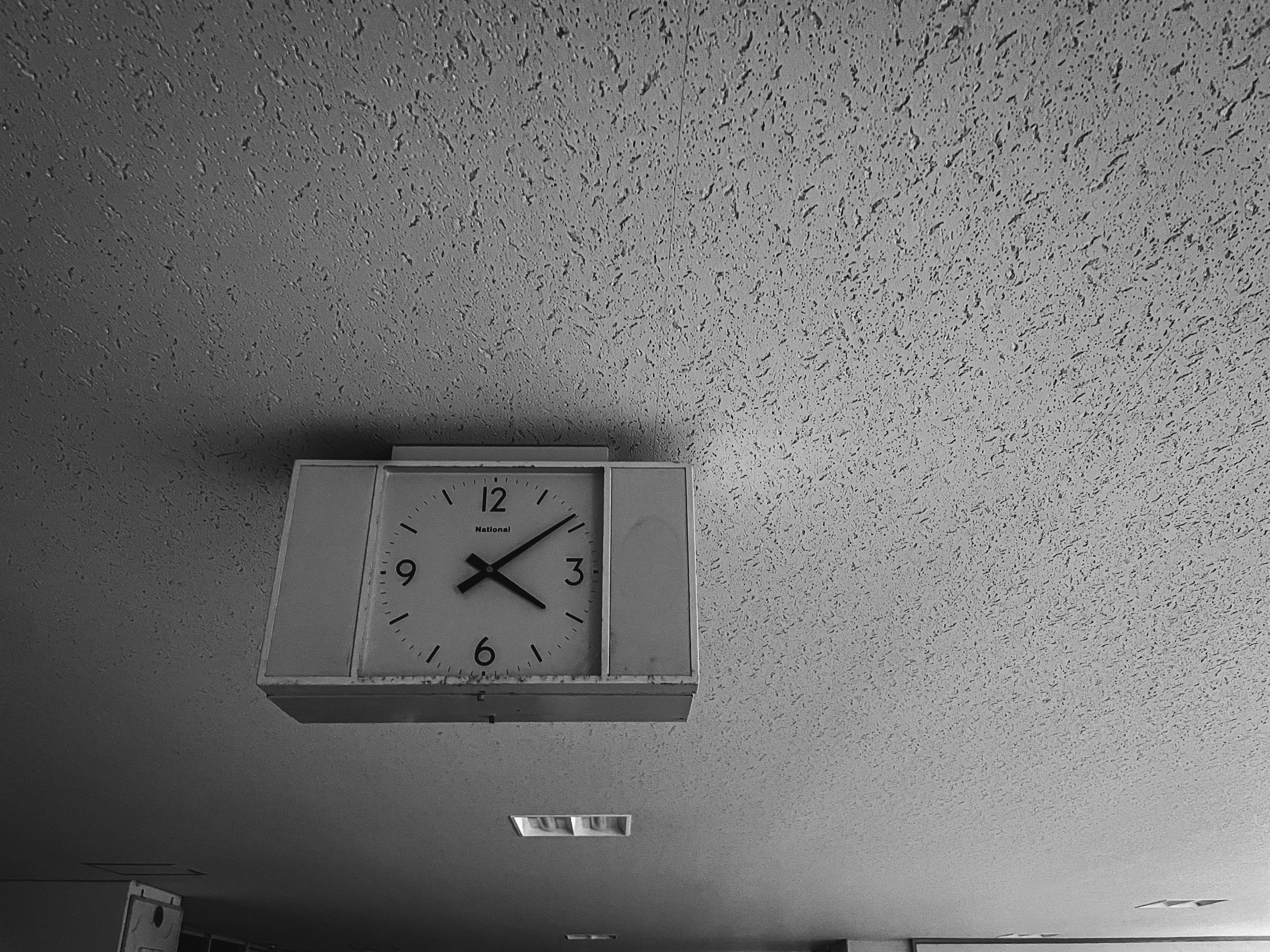 A simple white clock mounted on the ceiling in a black and white photo