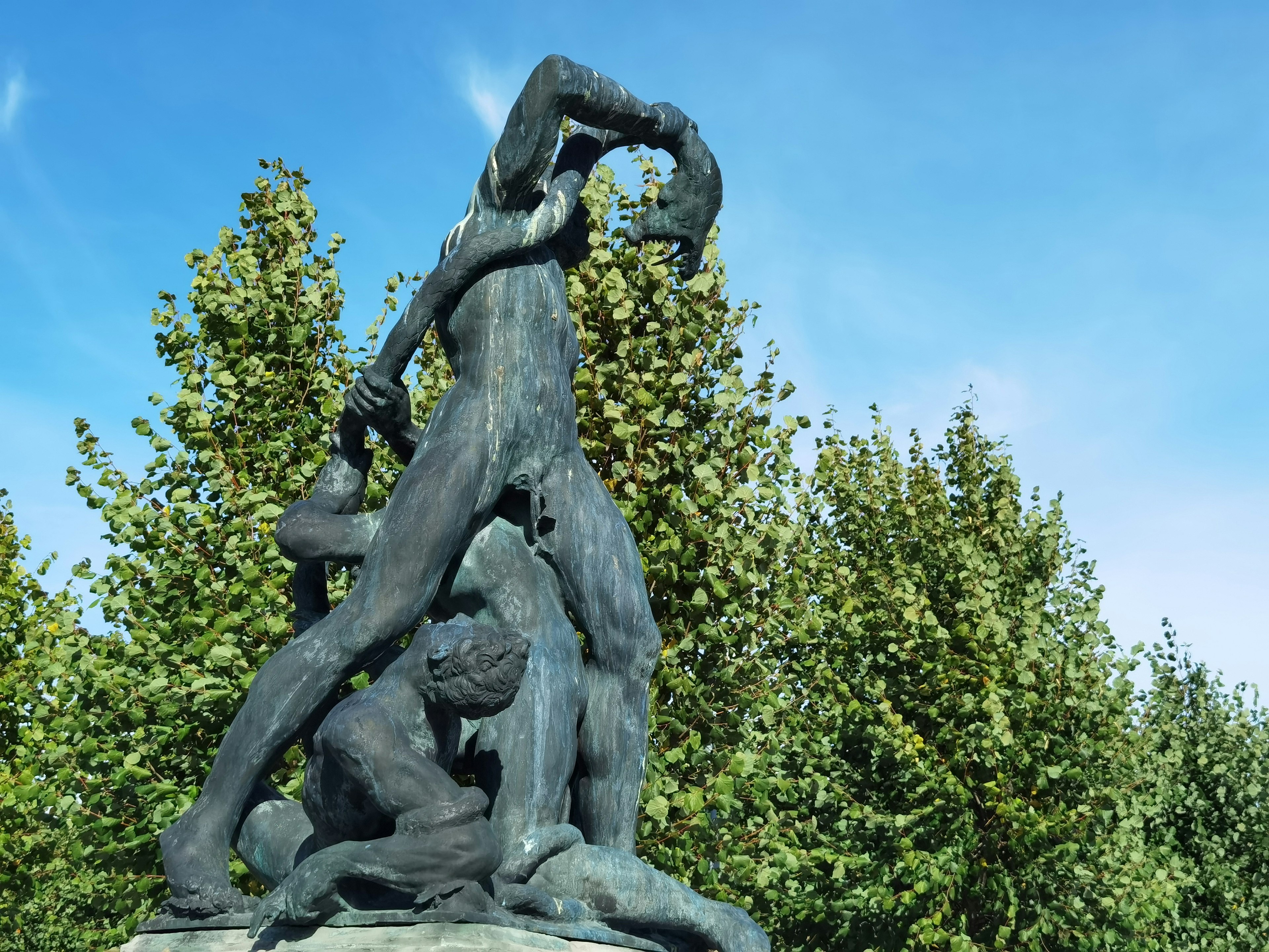 Groupe sculptural sous un ciel bleu avec des figures en postures fortes entourées d'arbres verts