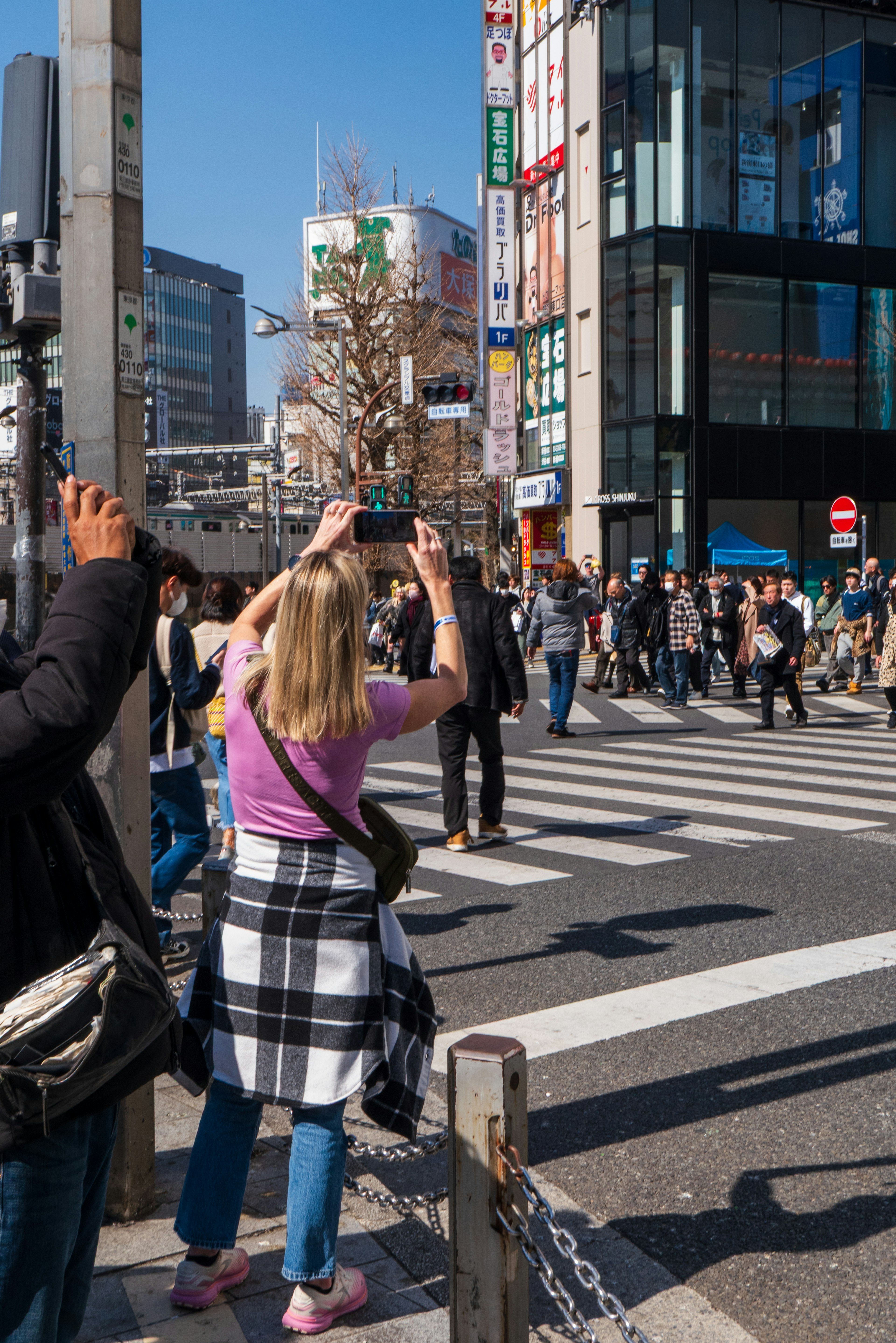 Woman taking a photo with smartphone at a busy crosswalk with pedestrians