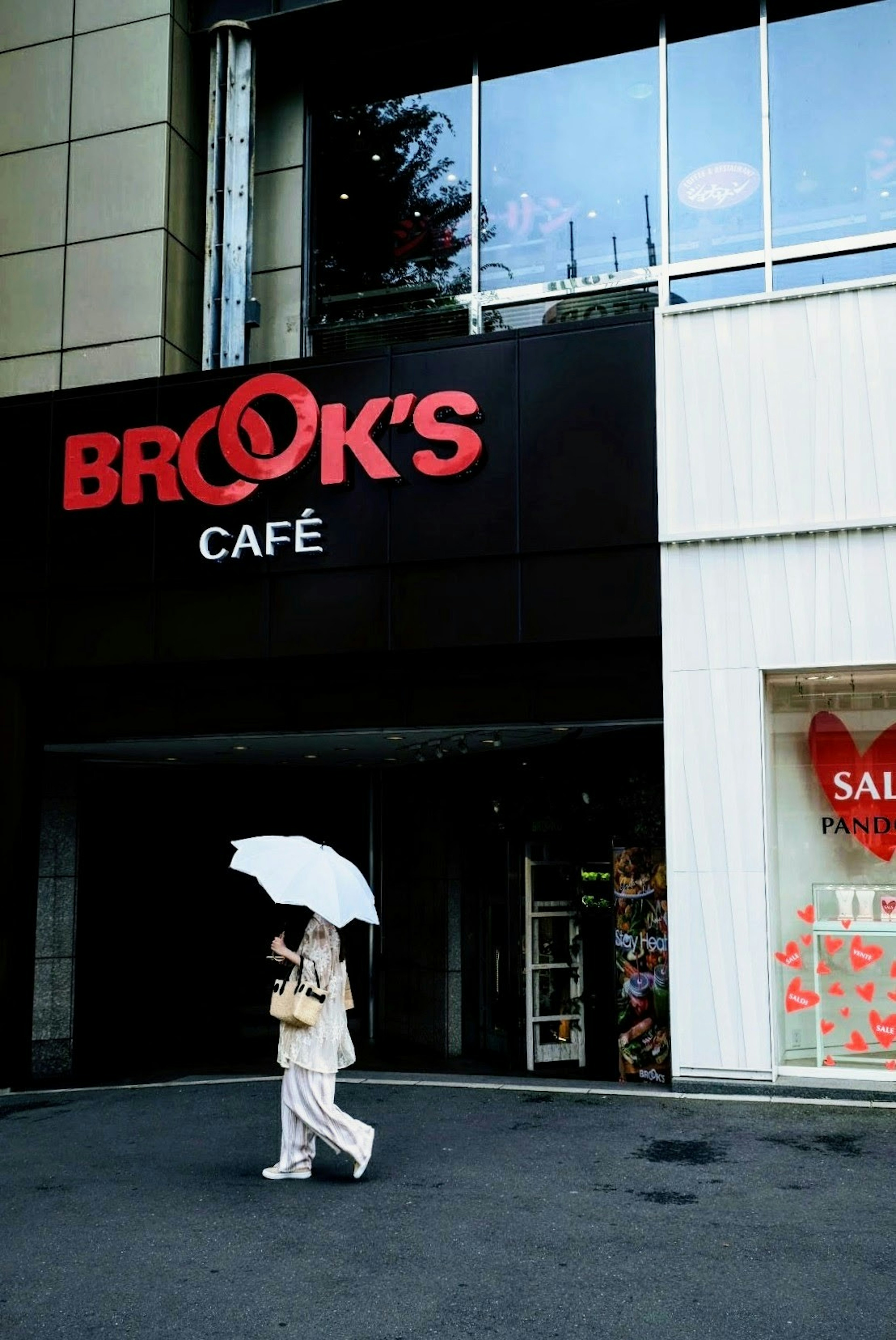 A woman walking in front of BROOK'S CAFÉ holding a white umbrella