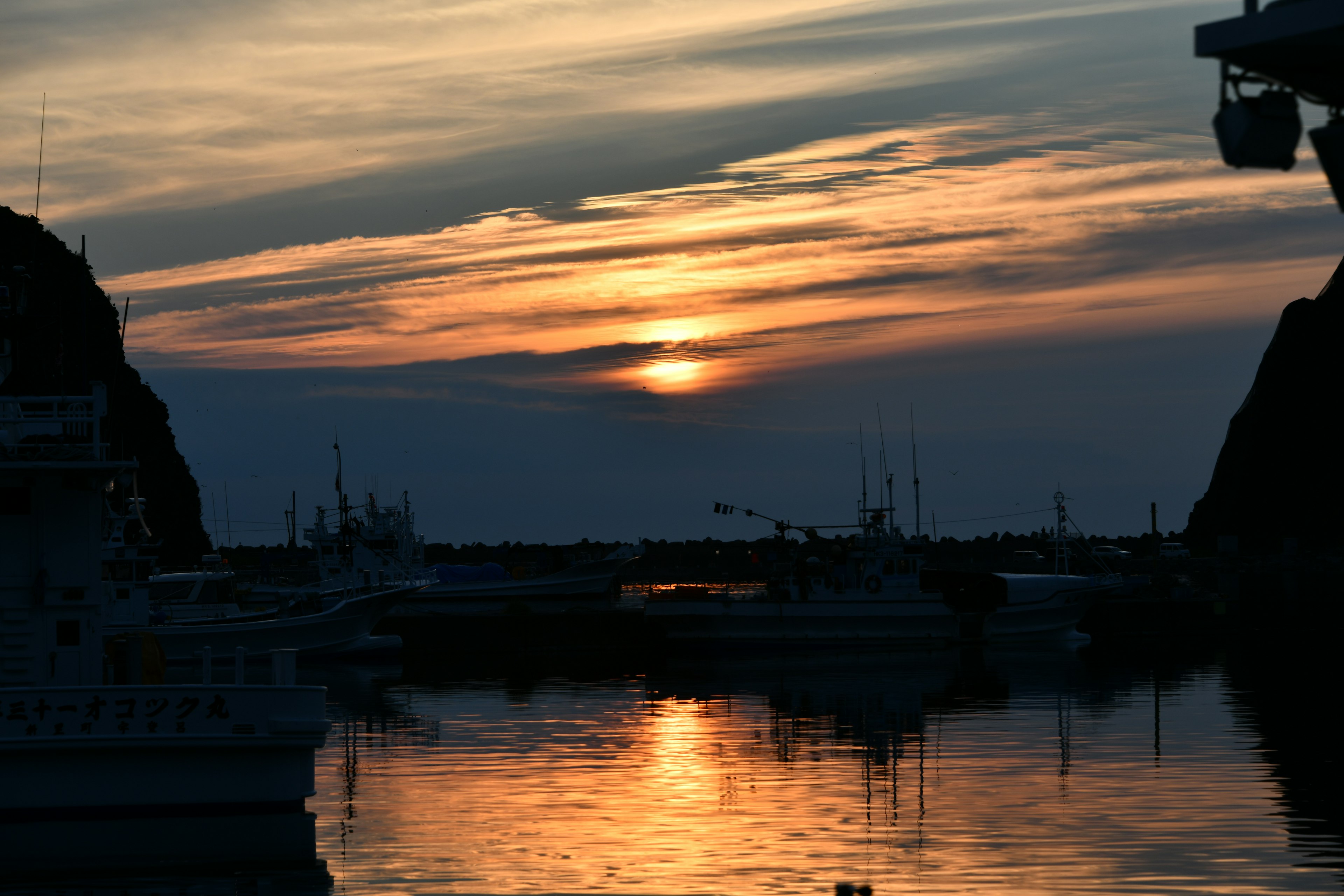 Hafenszene mit Sonnenuntergang, der sich auf dem Wasser spiegelt Silhouetten von Booten und Felsen