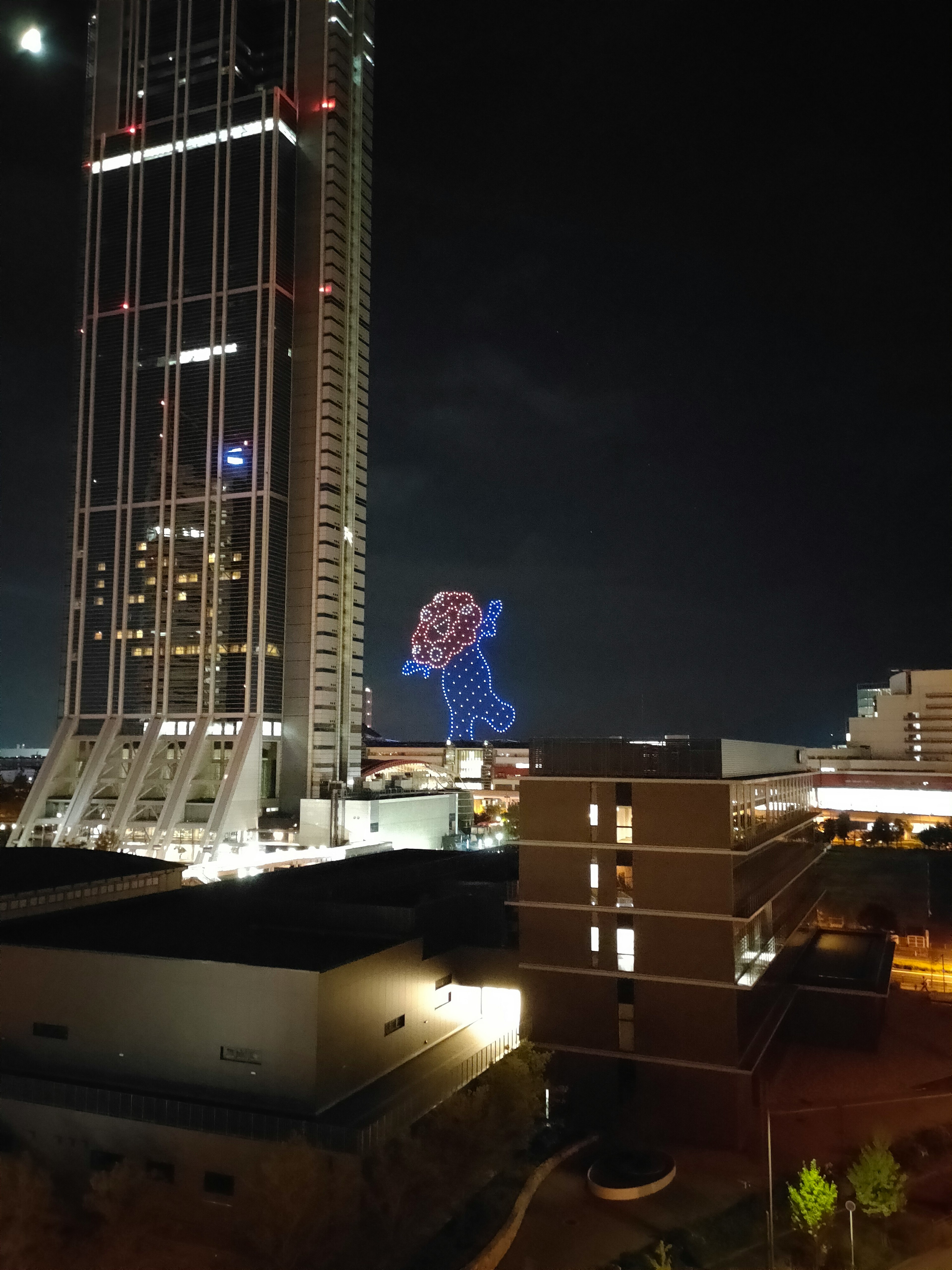 Large illuminated character in the night sky with a skyscraper