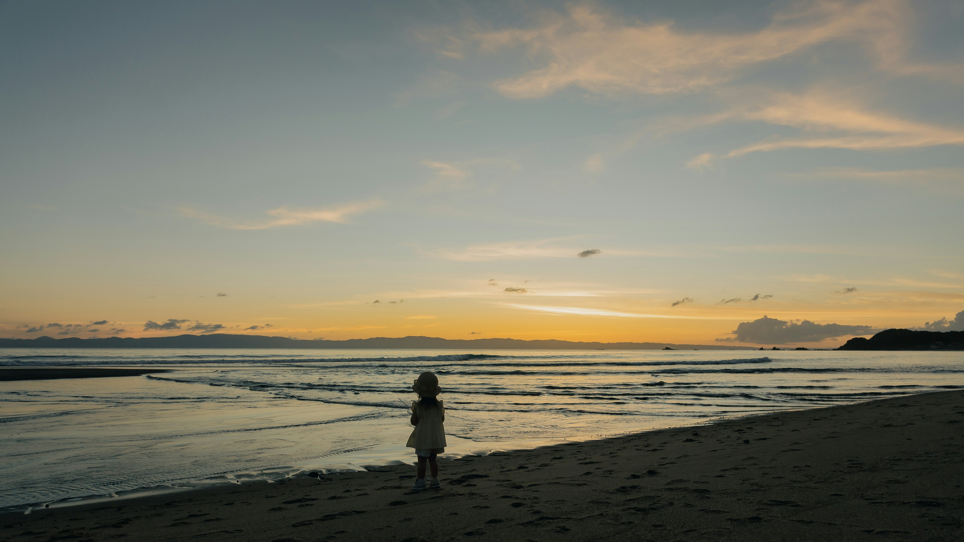 Silhouette d'un enfant contemplant un coucher de soleil sur la plage