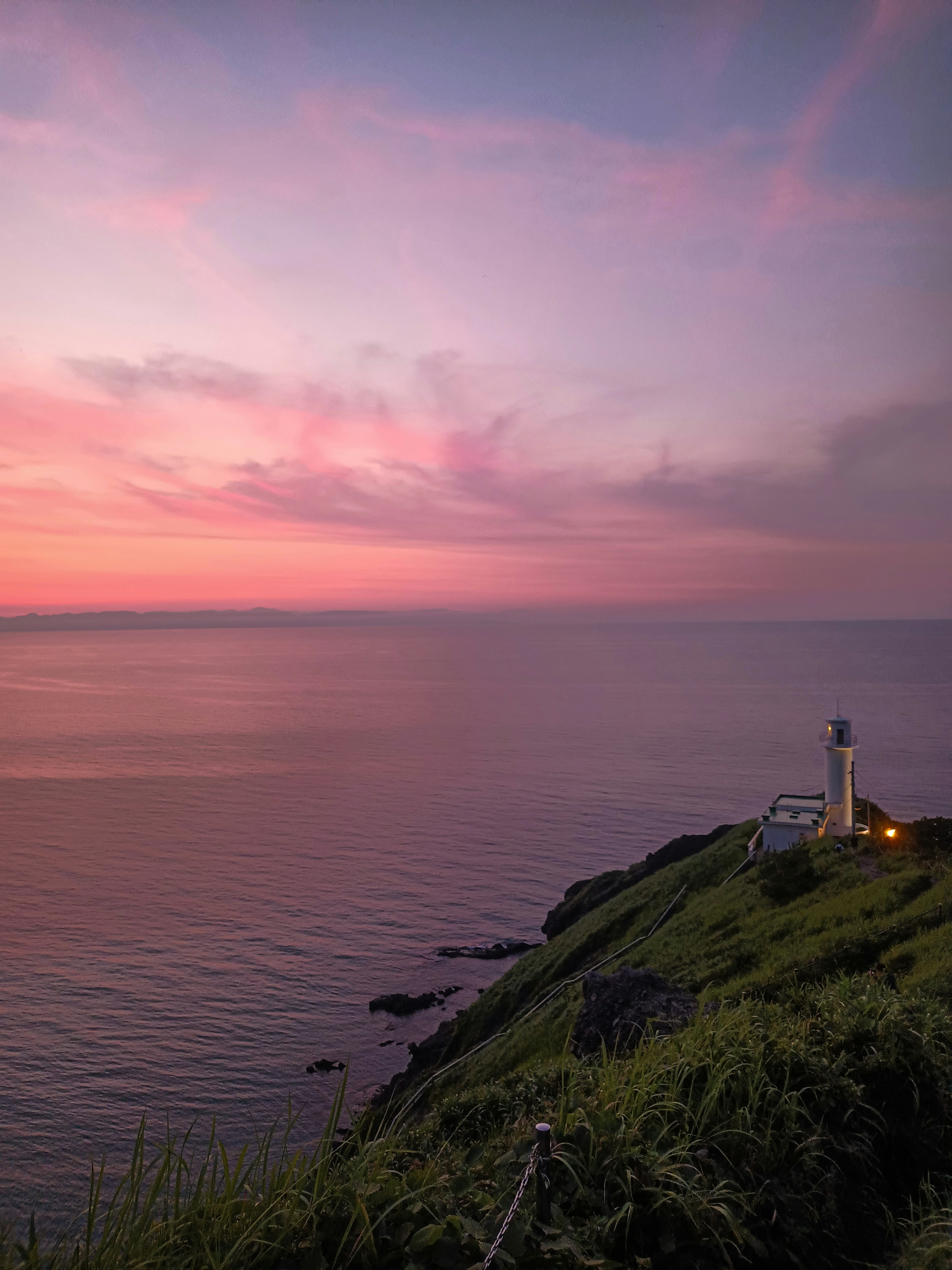 Lighthouse on a hillside overlooking a serene ocean at sunset