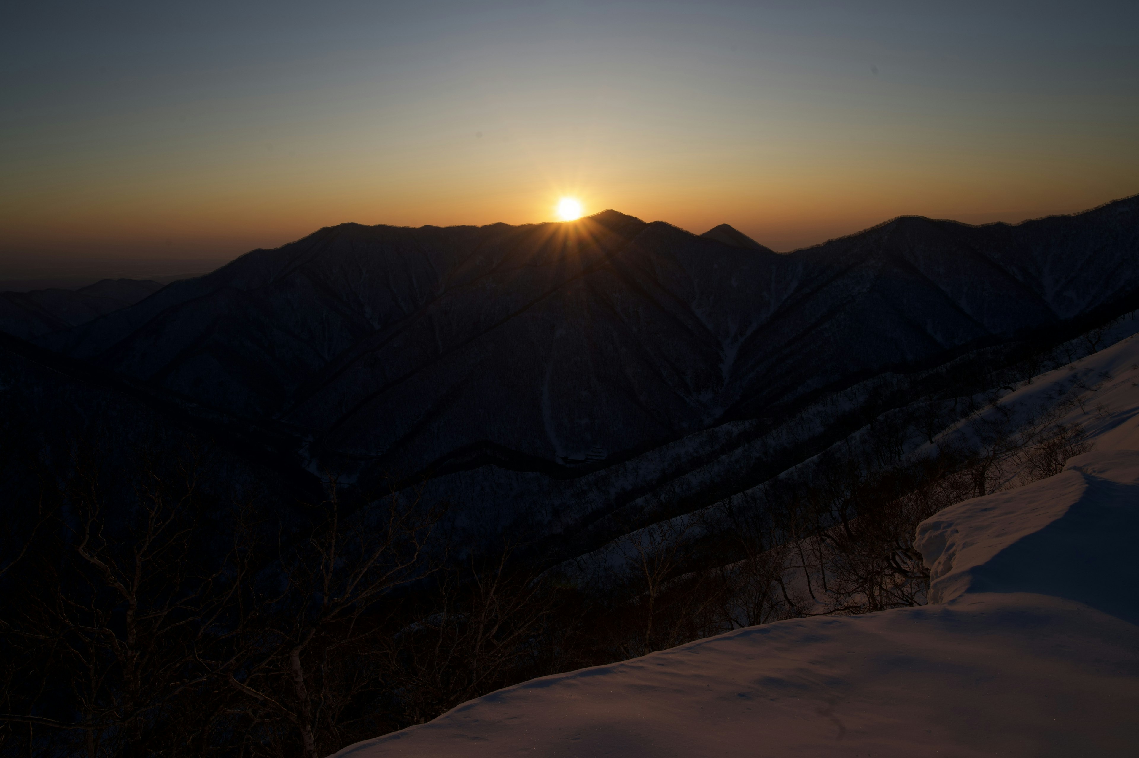 雪に覆われた山々の背後に昇る朝日