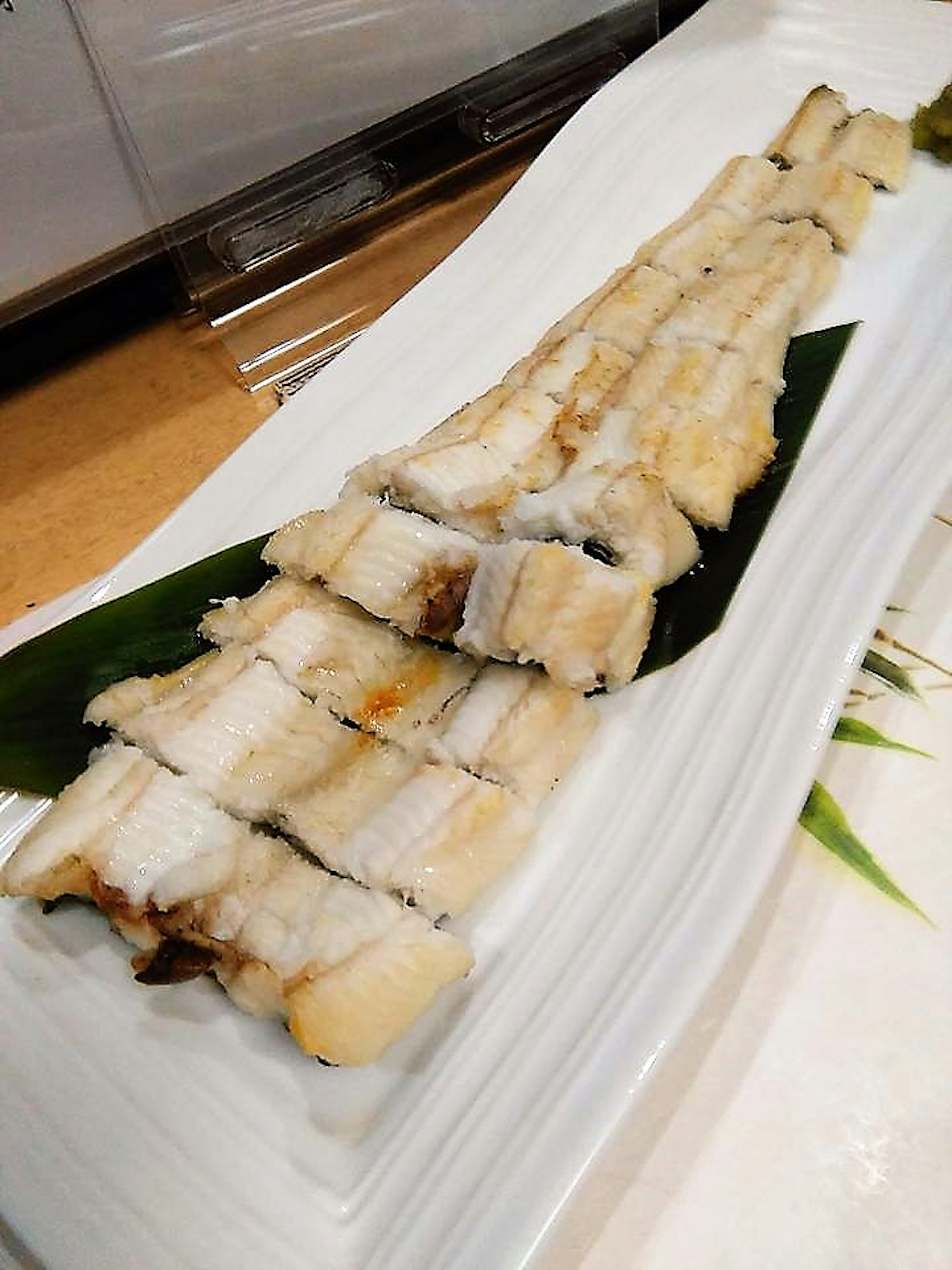 Anguila a la parrilla servida en un plato blanco con hojas verdes