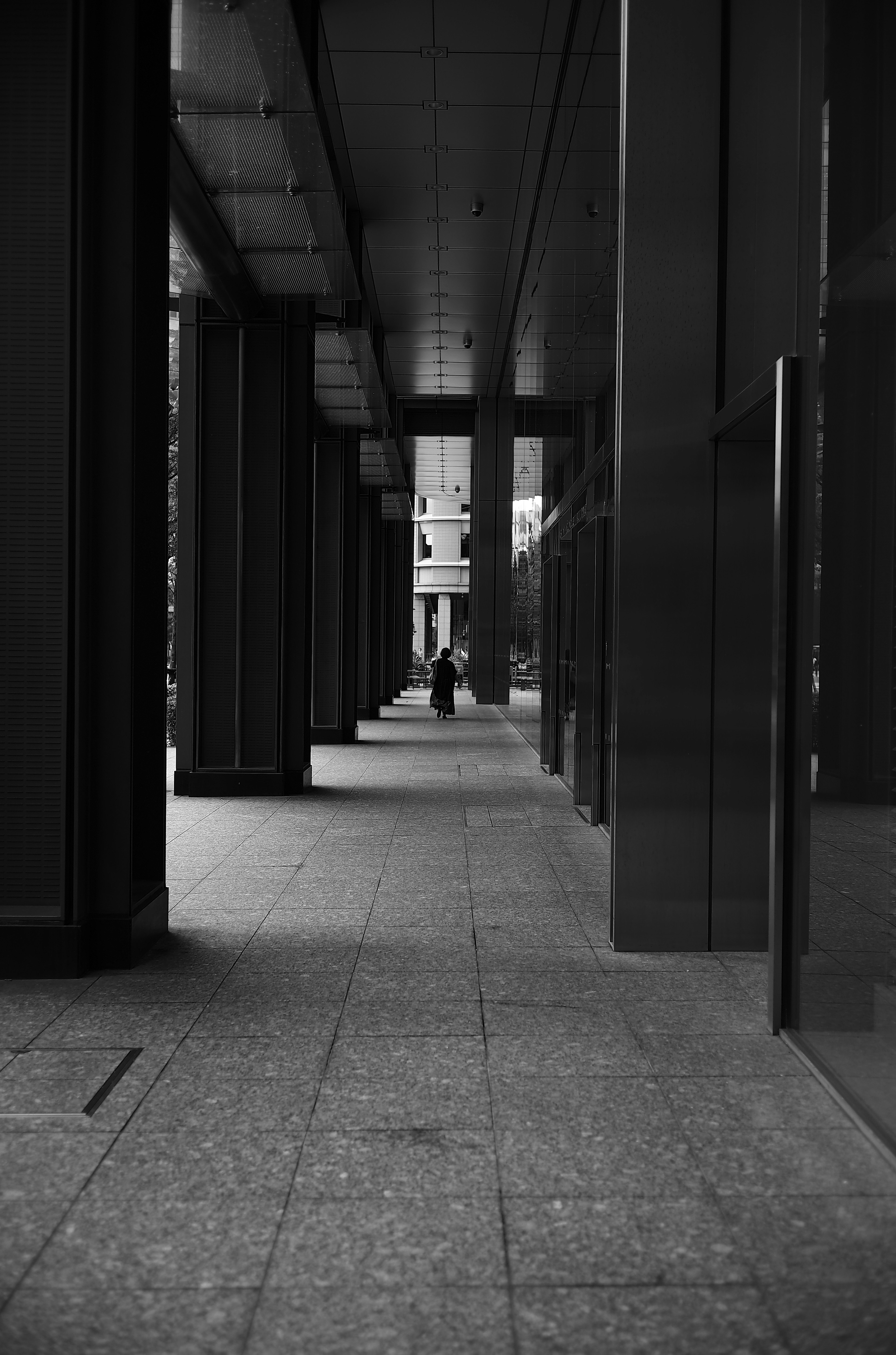 A person standing in a black and white urban corridor with columns