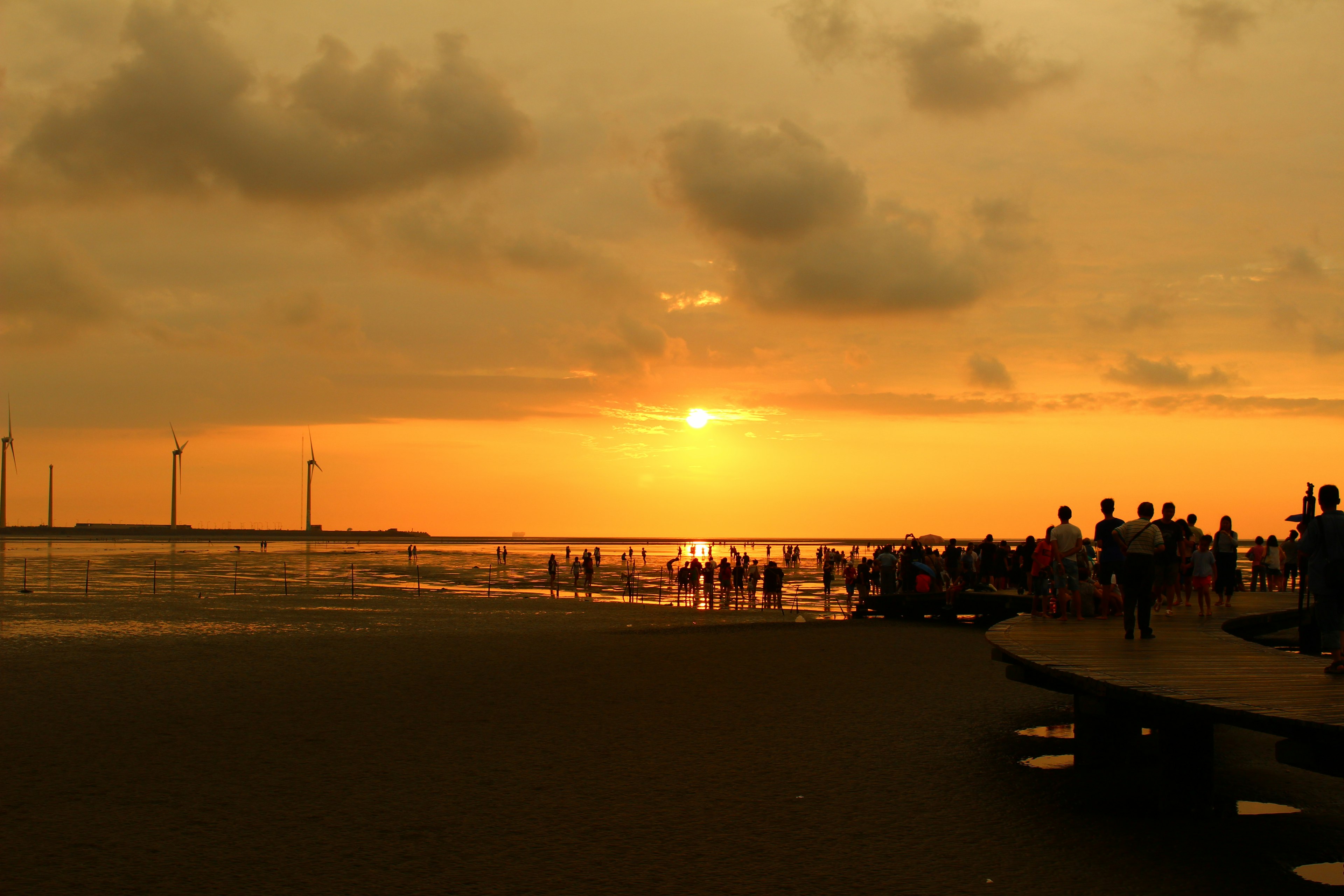 เงาของผู้คนที่ชายหาดในช่วงพระอาทิตย์ตกกับกังหันลม