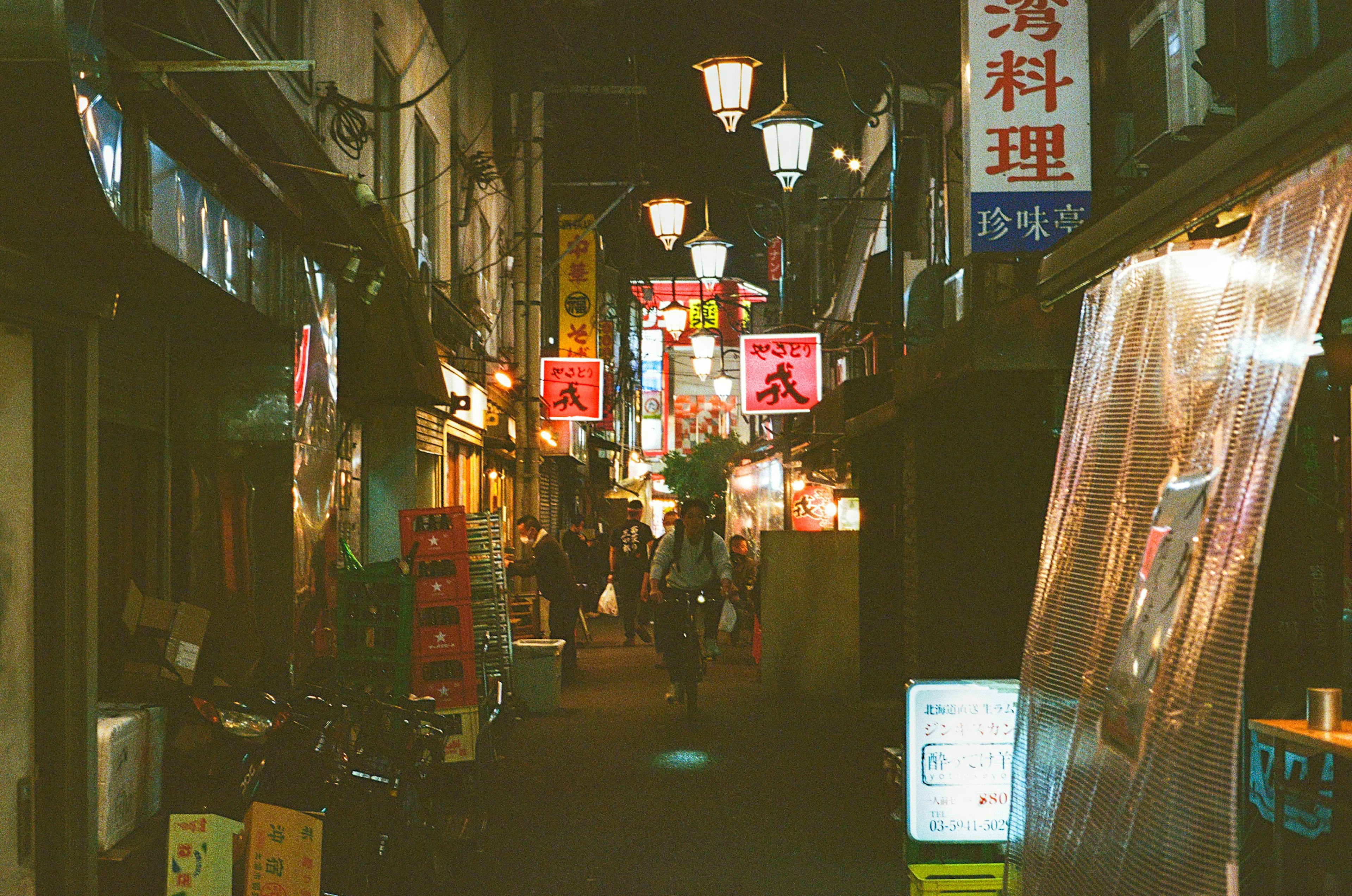 Ruelle étroite bordée de panneaux de restaurants et de lanternes