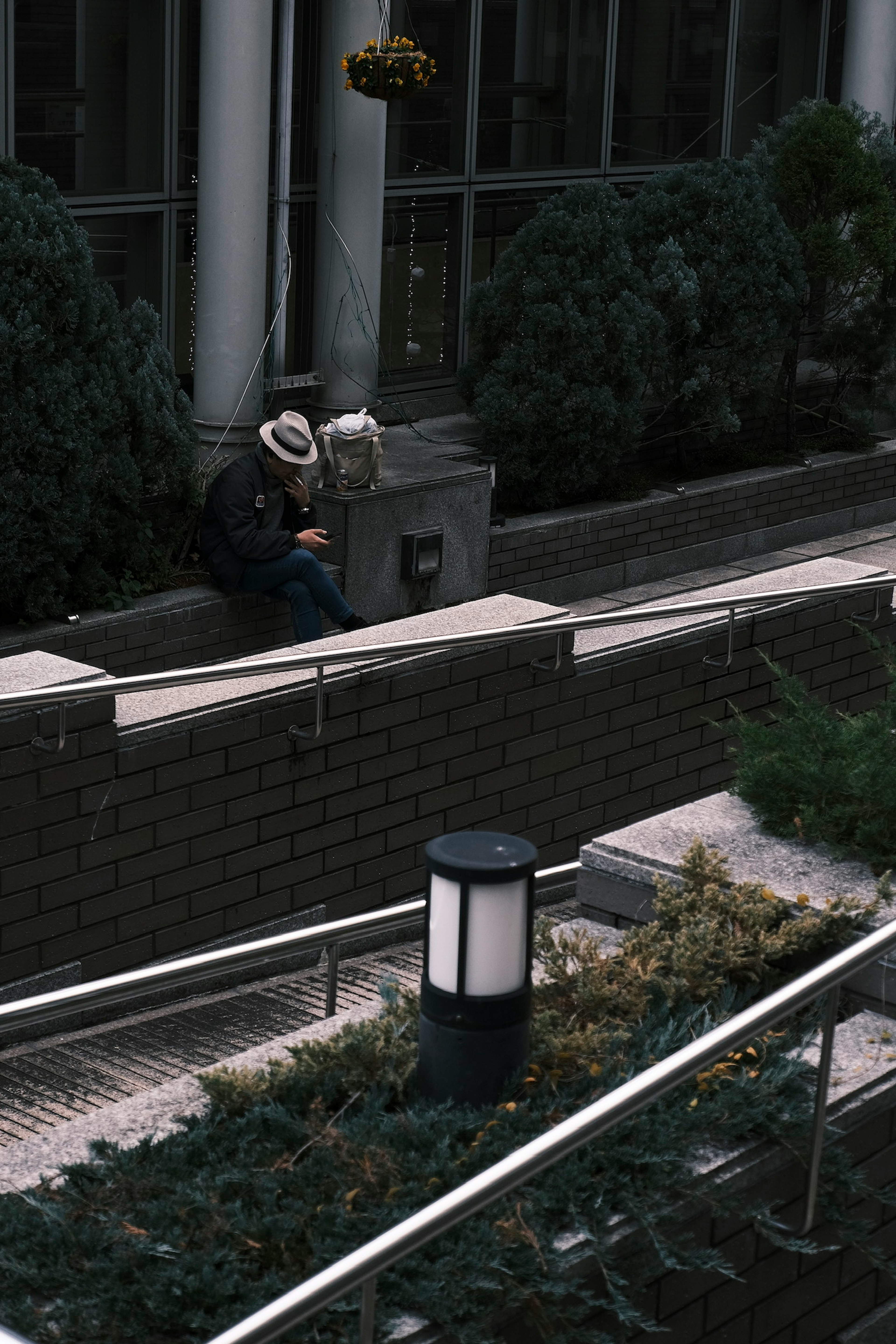 A man wearing a hat sitting on a bench in a garden area