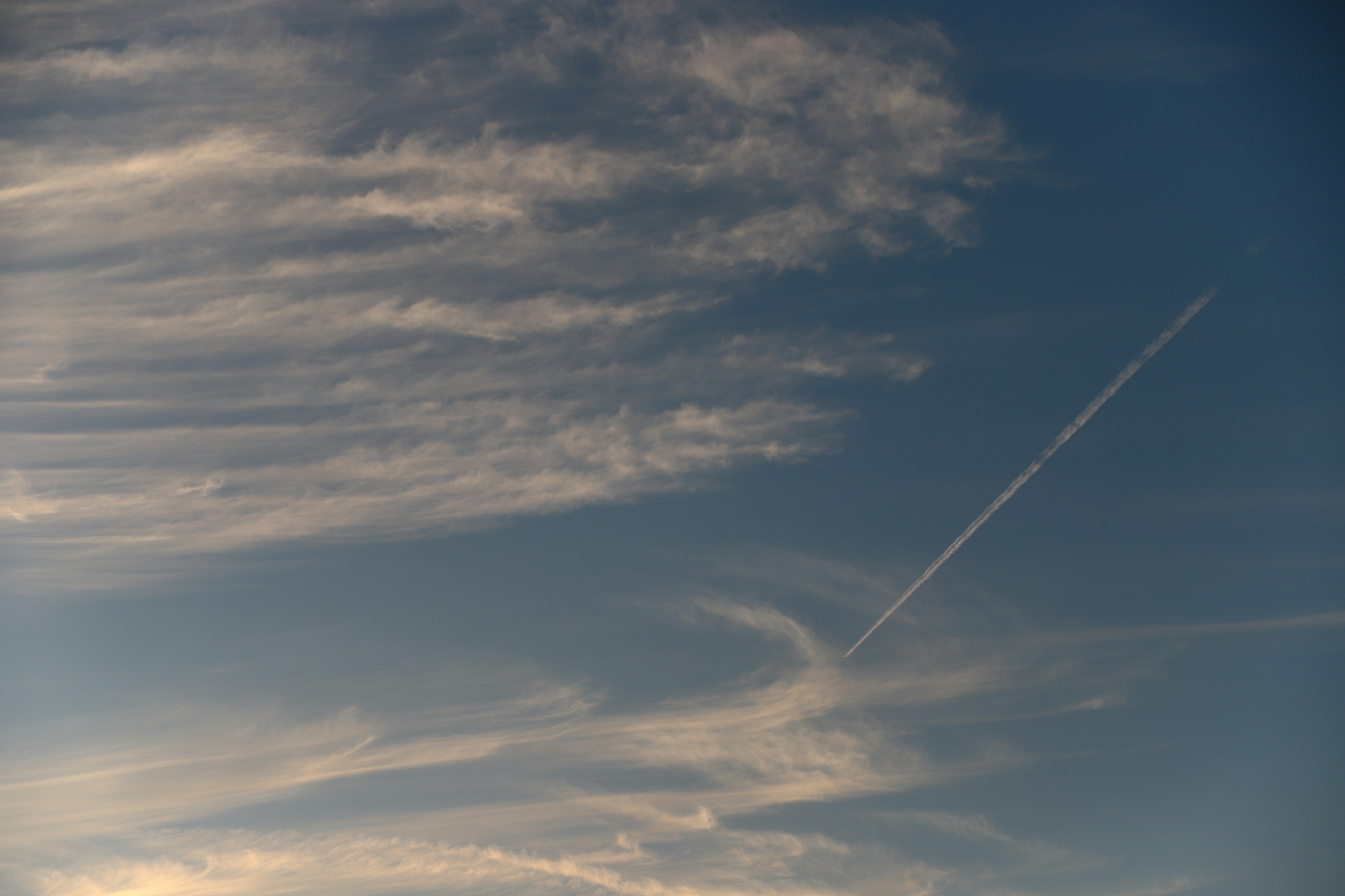 A serene sky with wispy clouds and a visible contrail