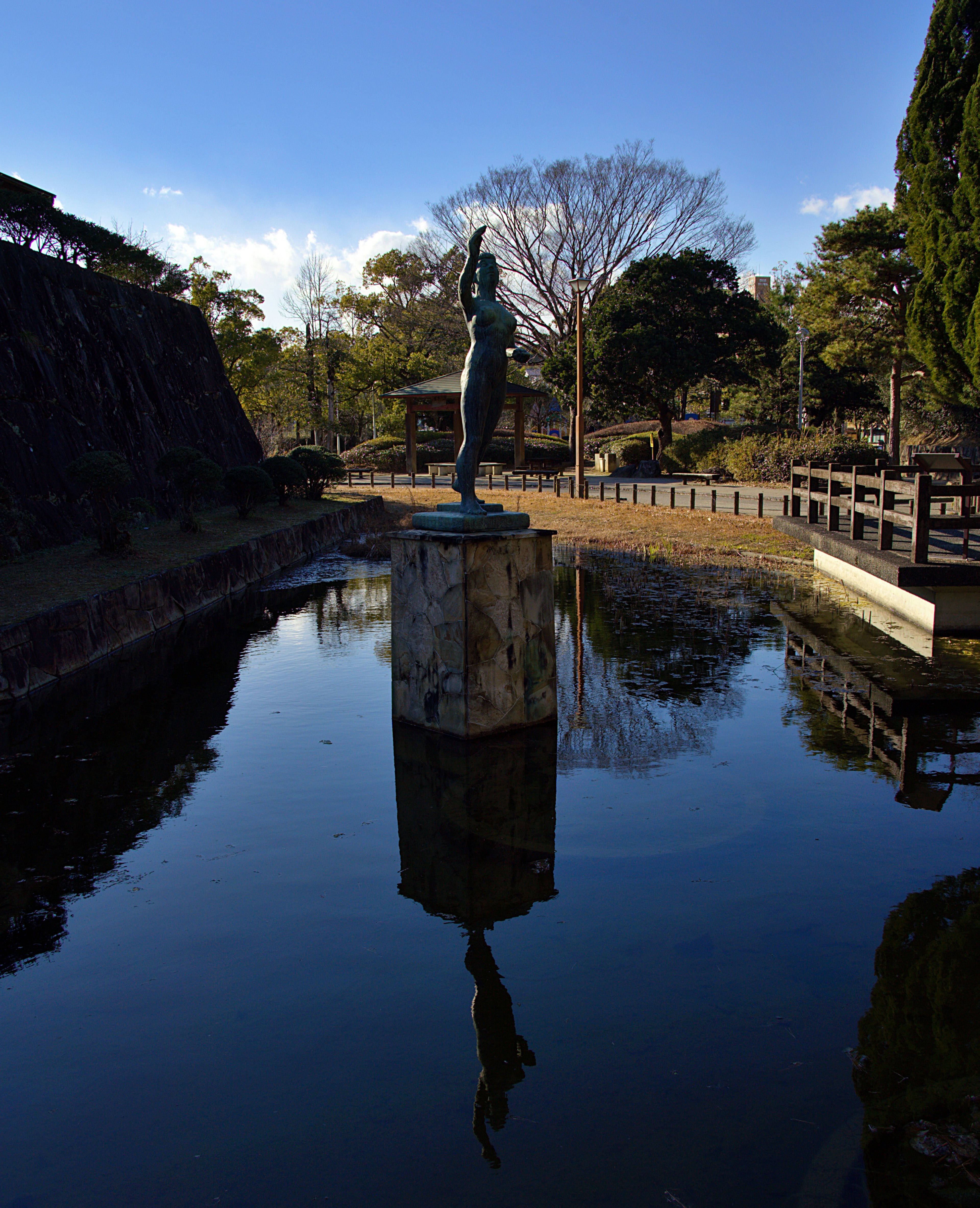 静かな公園の池に立つ彫像の反射