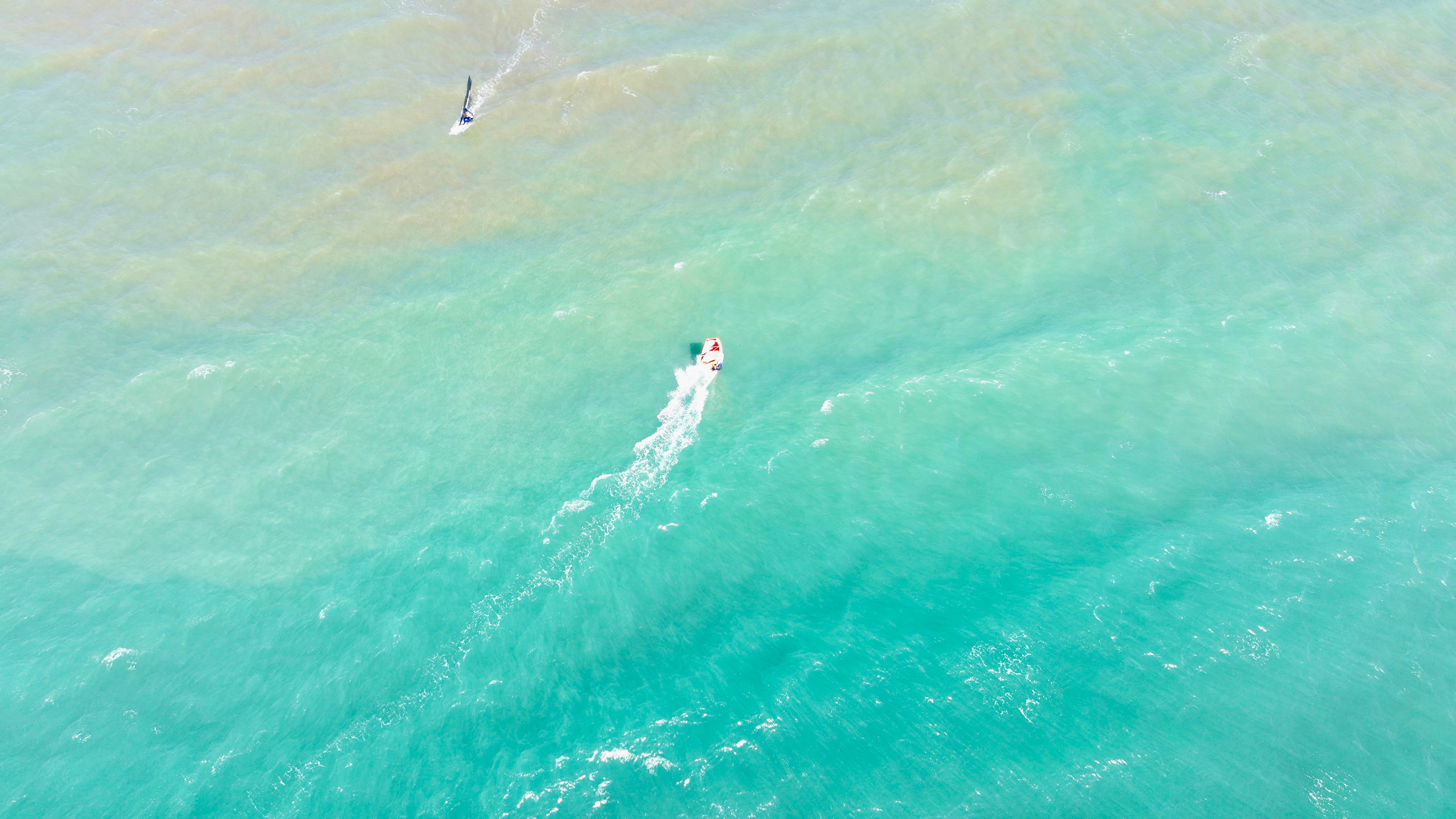 Ein Boot gleitet über blaues Wasser mit einer Person, die surft