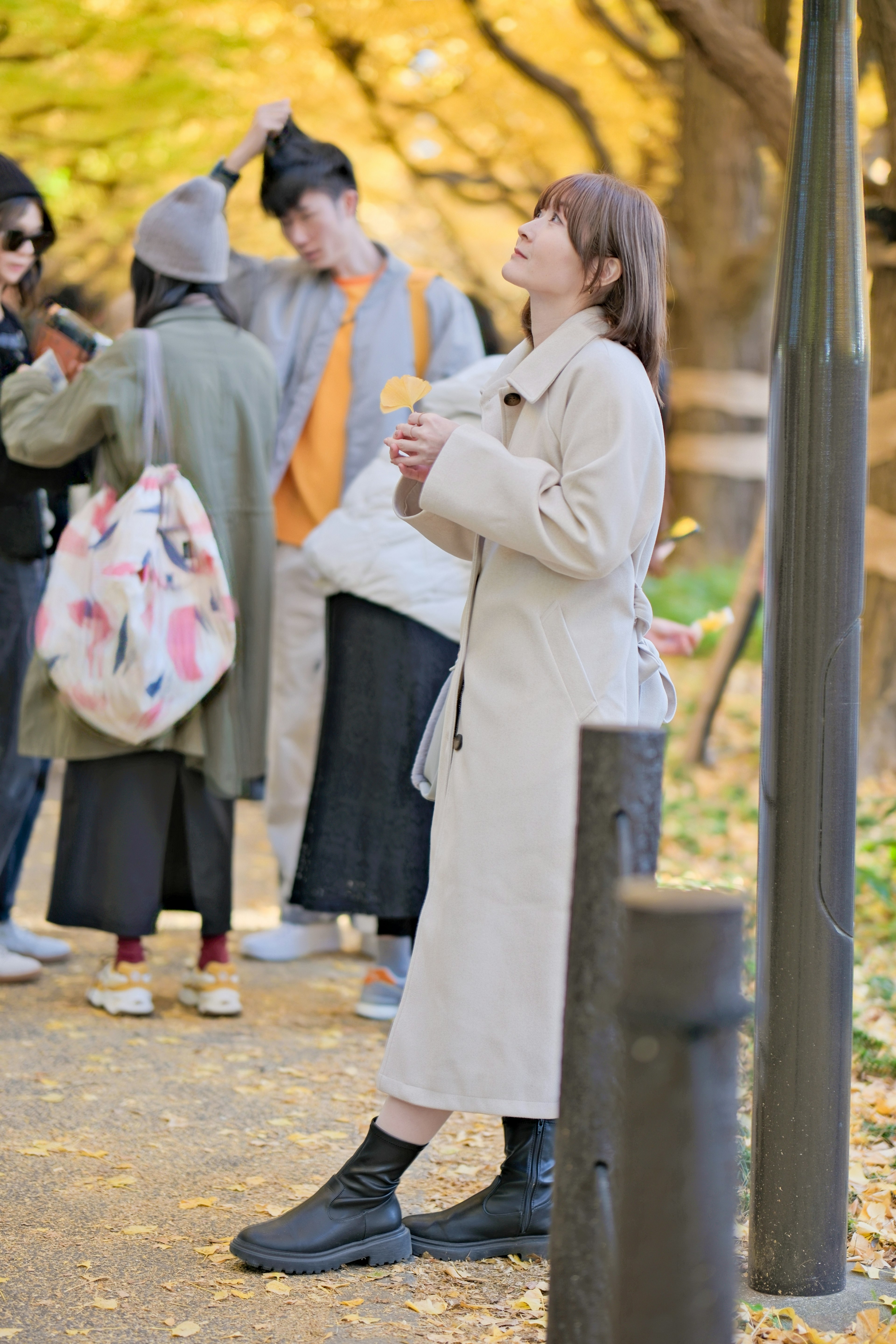 公園でコートを着た女性が立っている周りには友人たちがいる