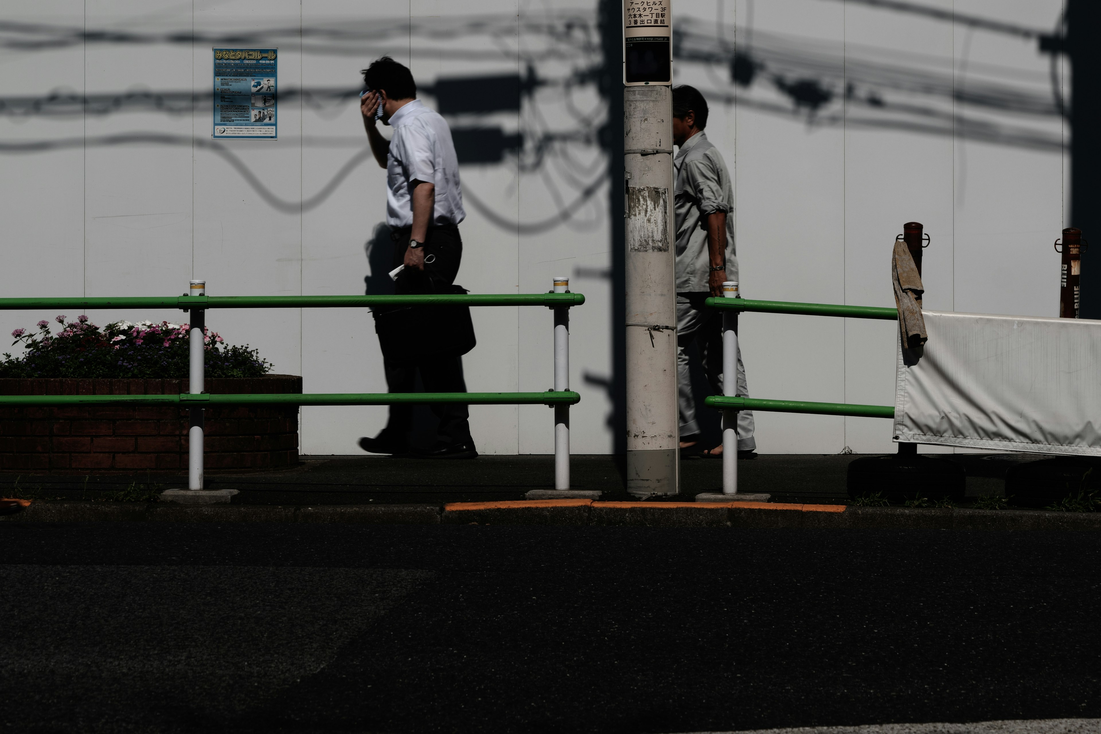 Two men walking in an urban setting with green railings and a white wall in the background