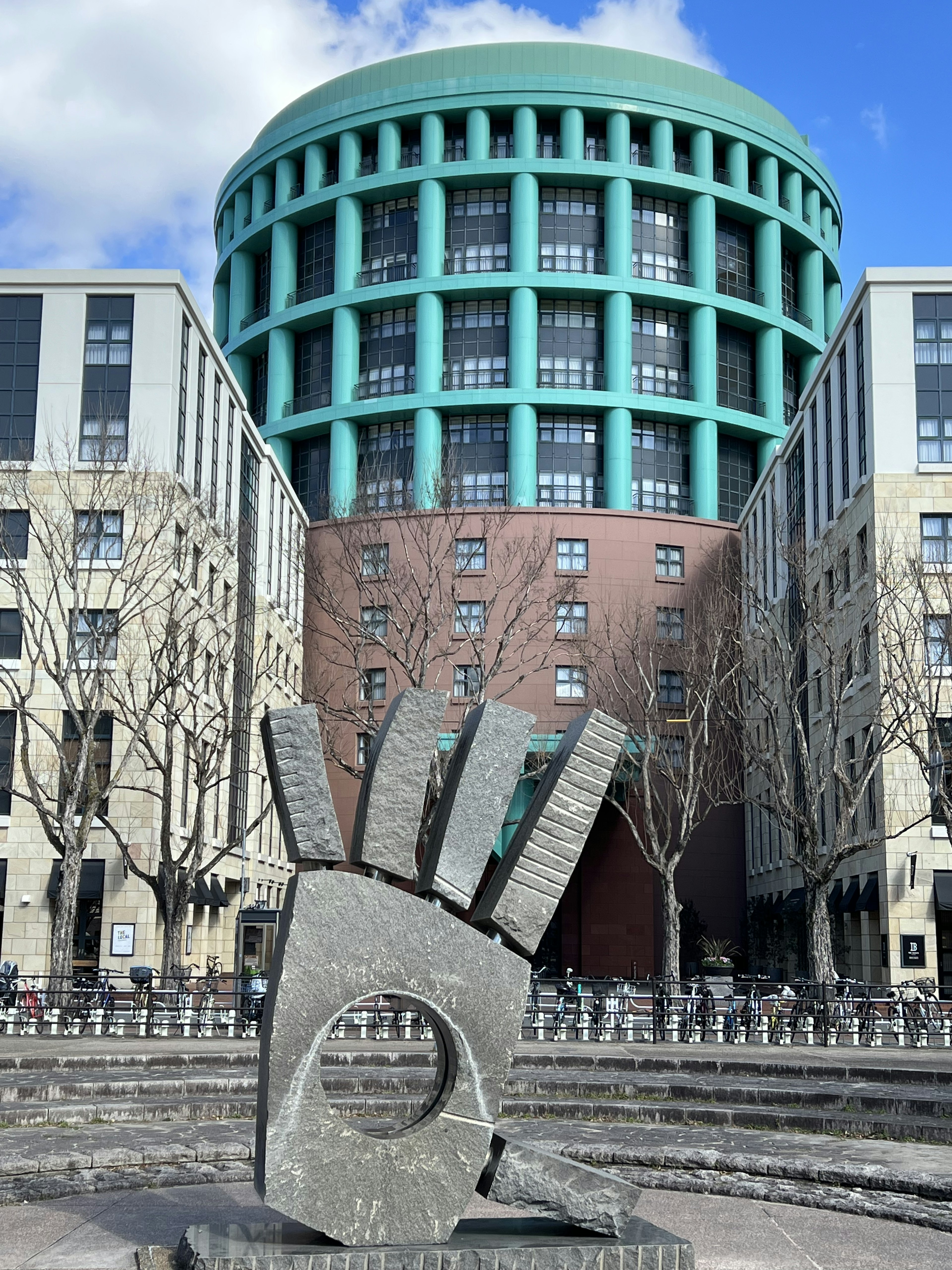 青い屋根の現代的な建物と石の彫刻が特徴の都市風景