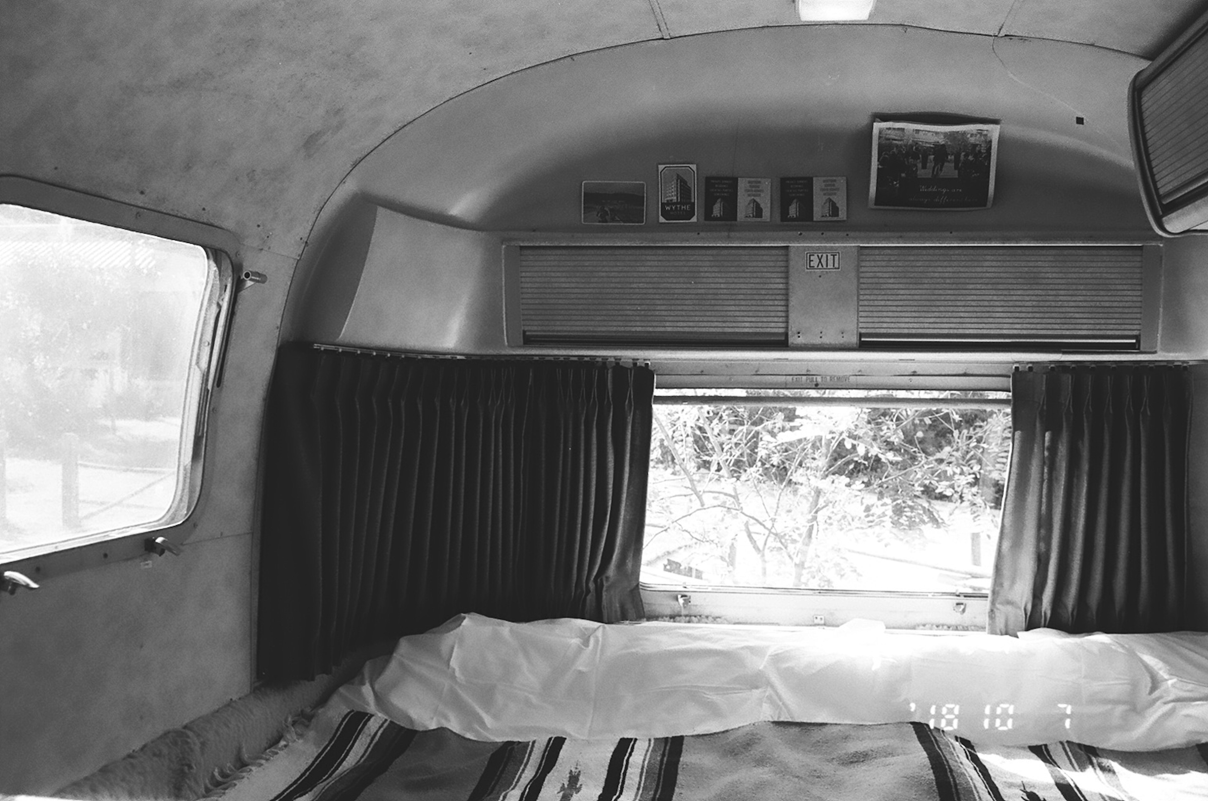 Interior trailer vintage hitam putih dengan jendela dan tirai serta tempat tidur