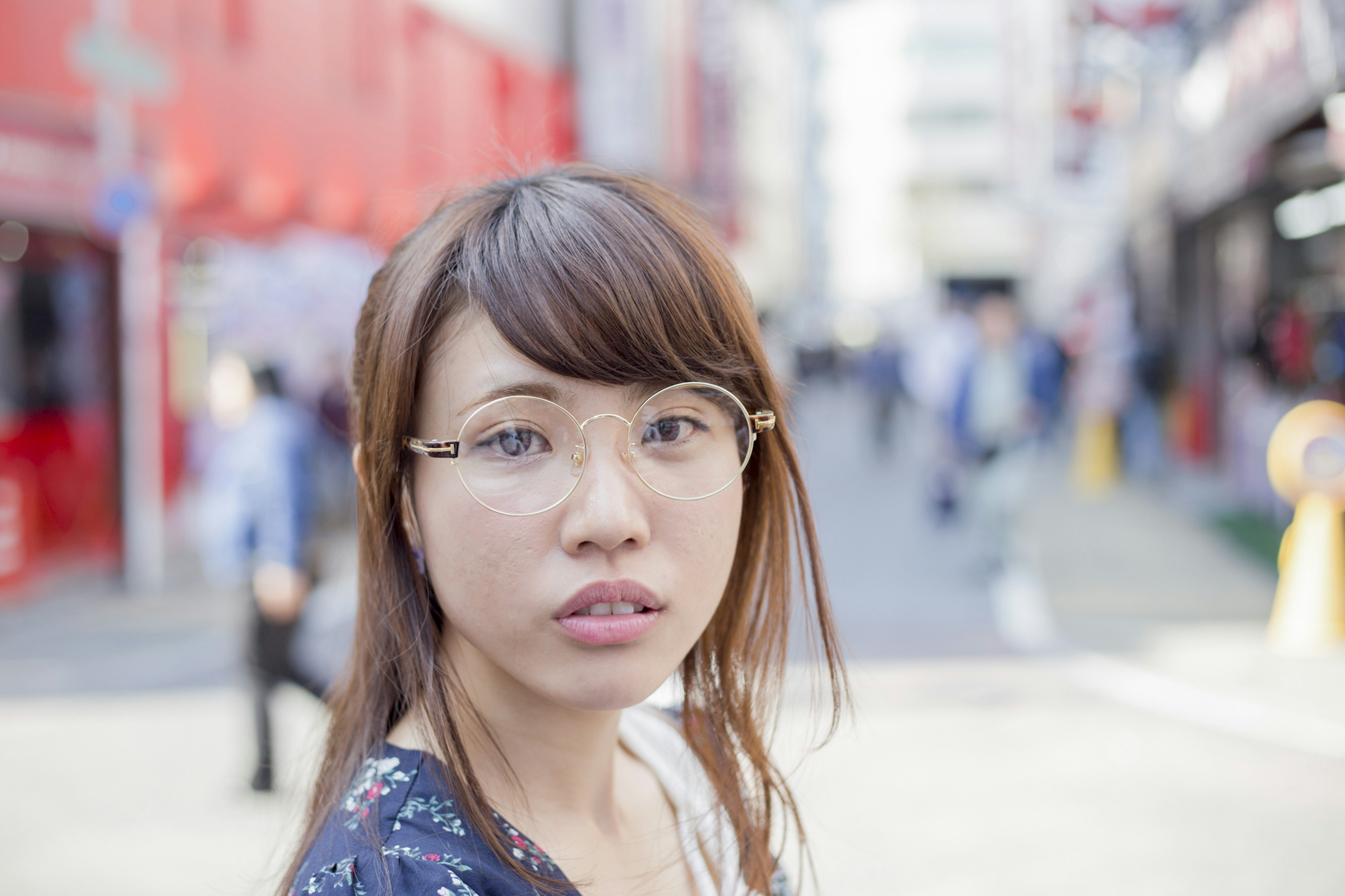 街中でカメラを見つめる女性のポートレート 背景には人々と赤い建物が見える