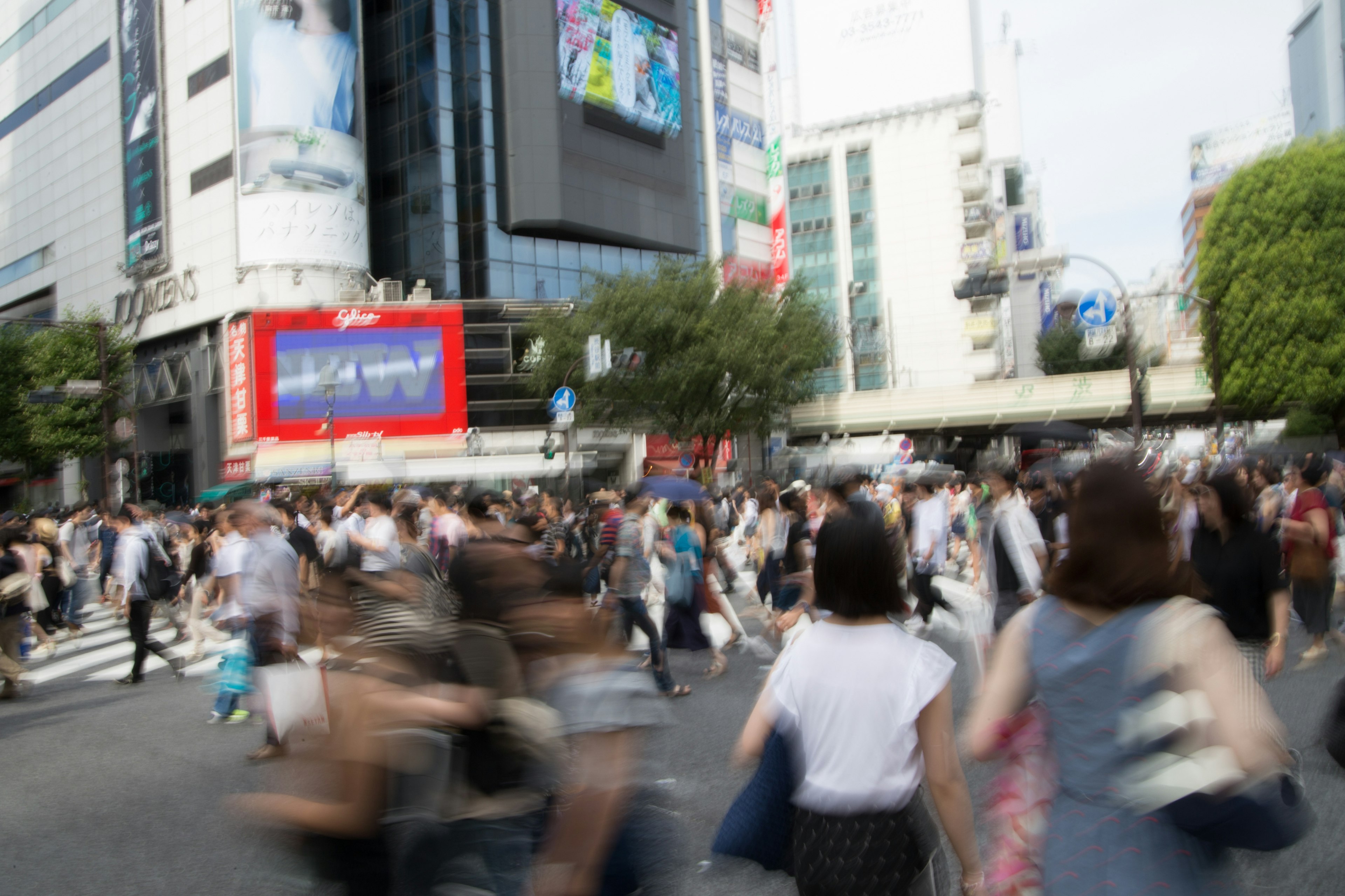 Folla di persone che attraversano l'incrocio di Shibuya con edifici e pubblicità sullo sfondo