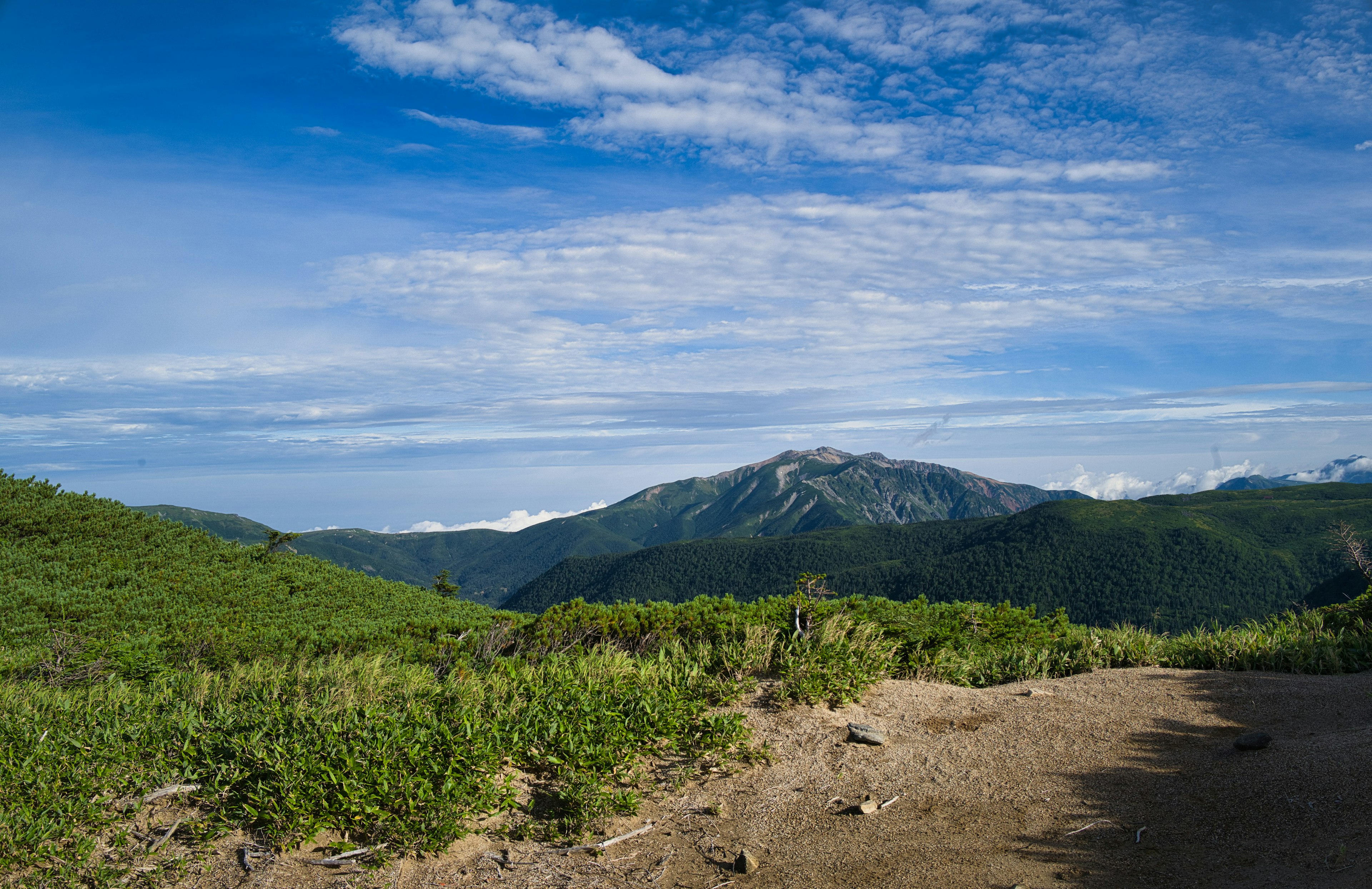 Berglandschaft mit grünen Feldern unter blauem Himmel und Wolken