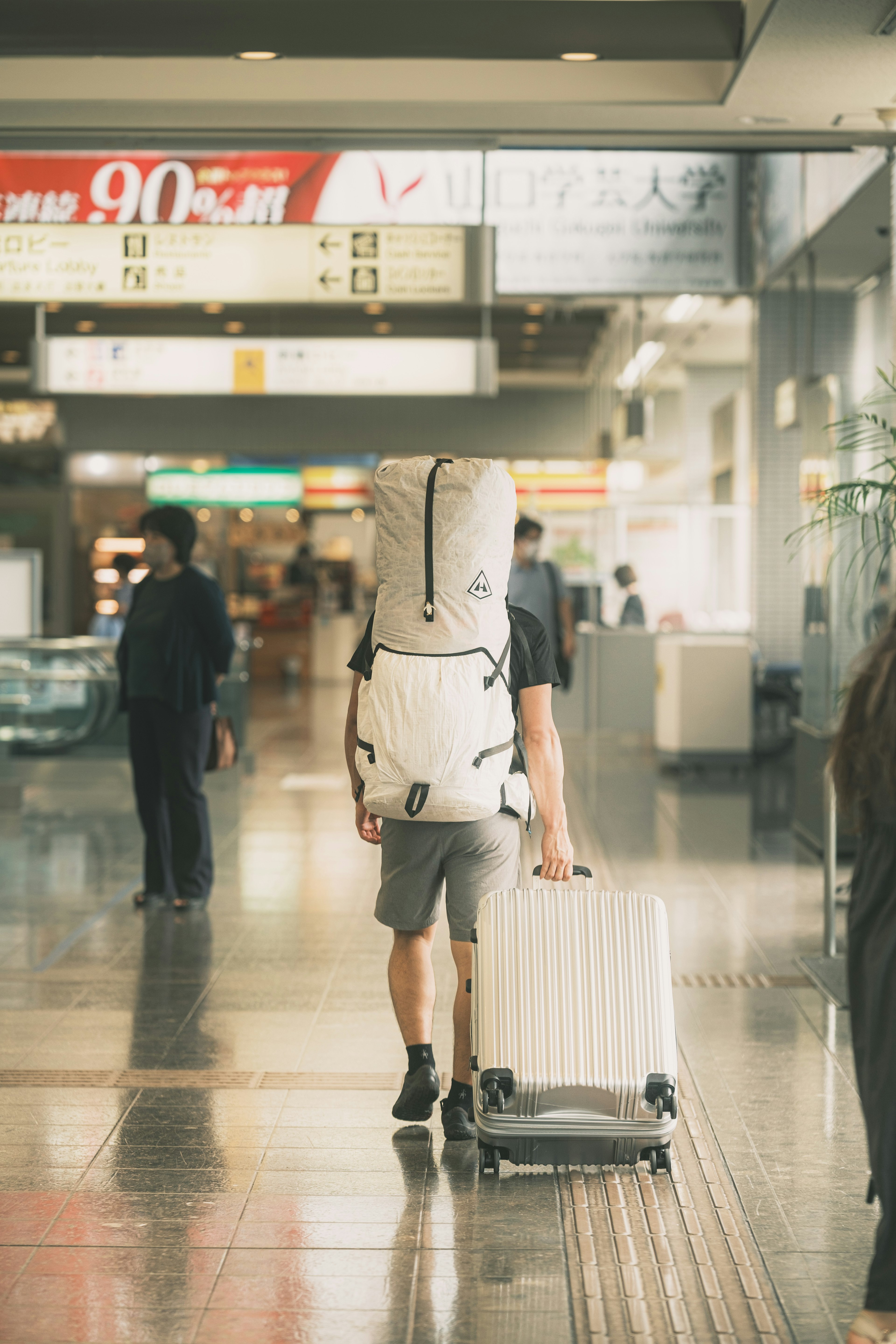 Traveler carrying a large backpack and pulling a suitcase in an airport