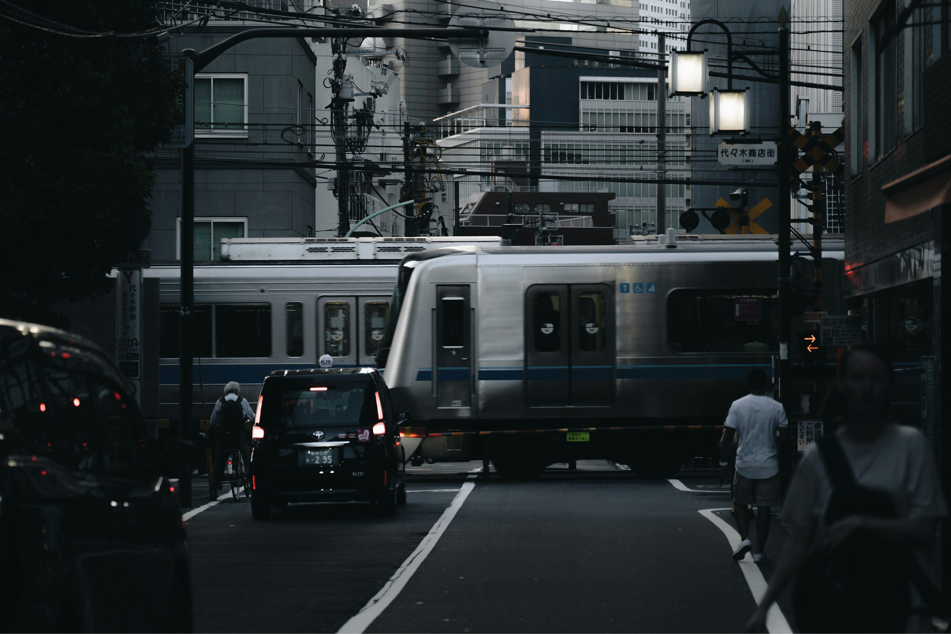 Scene of a train crossing a dark street with cars and pedestrians