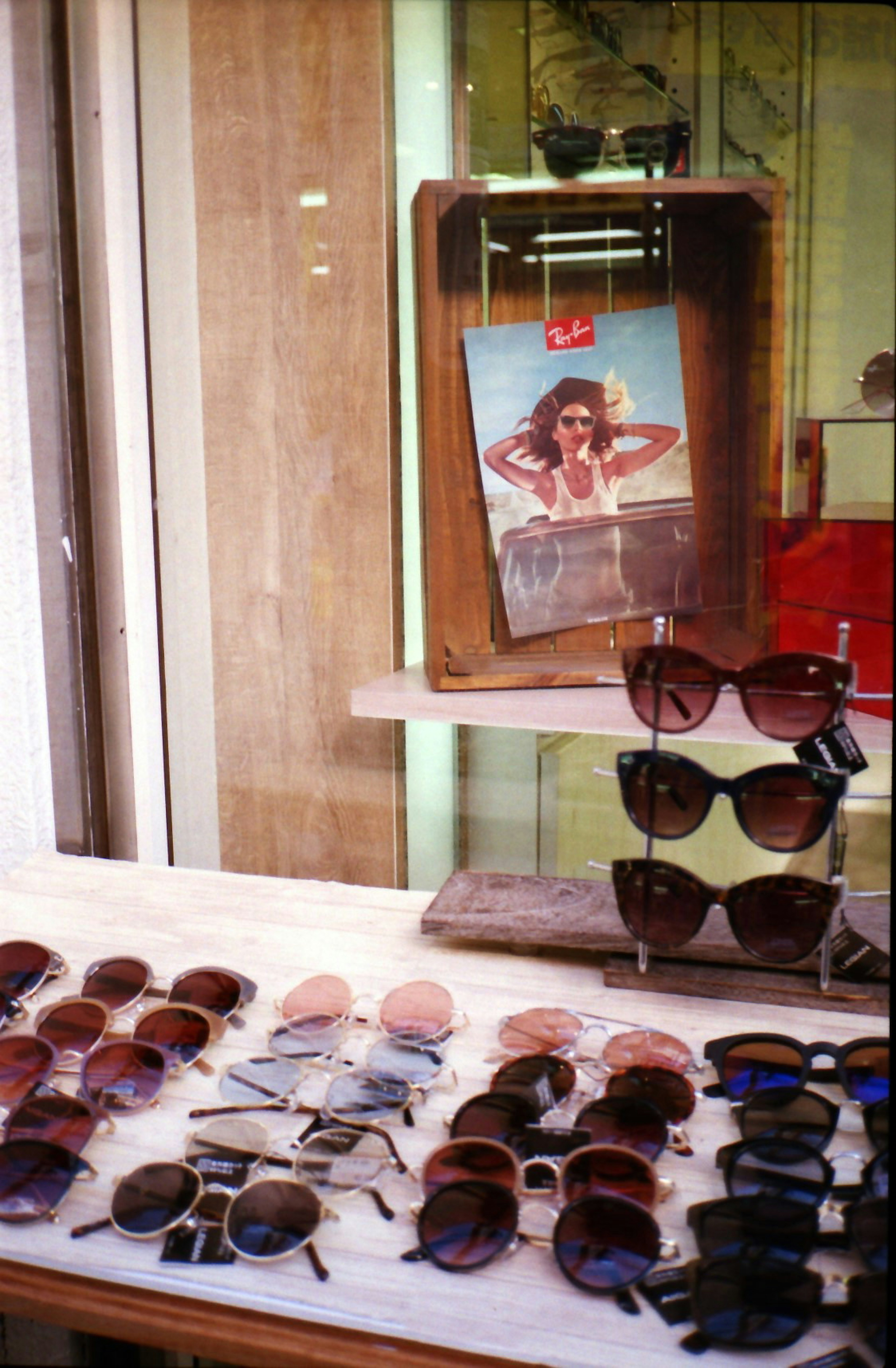 Display of sunglasses in a shop window with a poster in the background