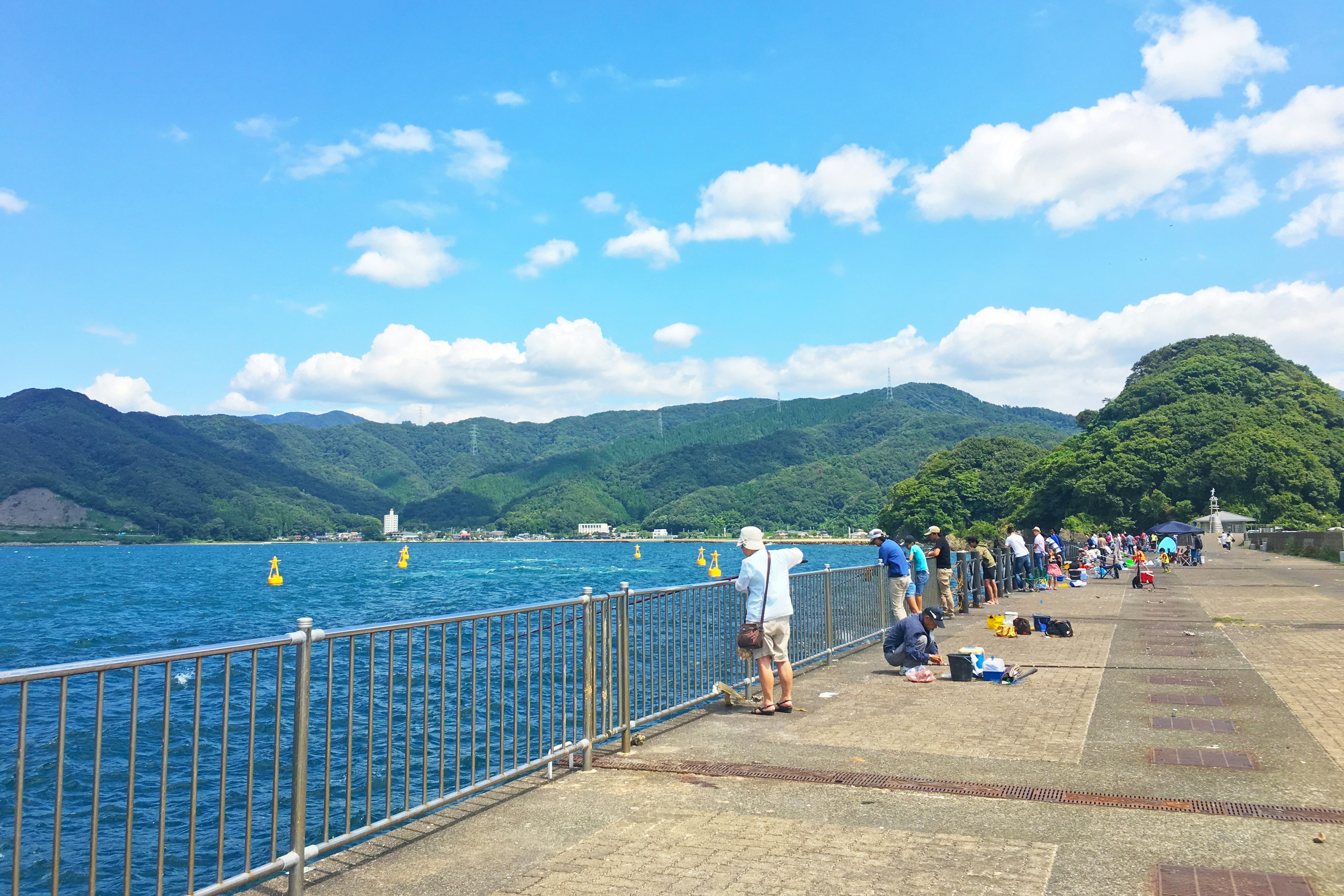 Fishermen along a pier with blue sea and mountains in the background