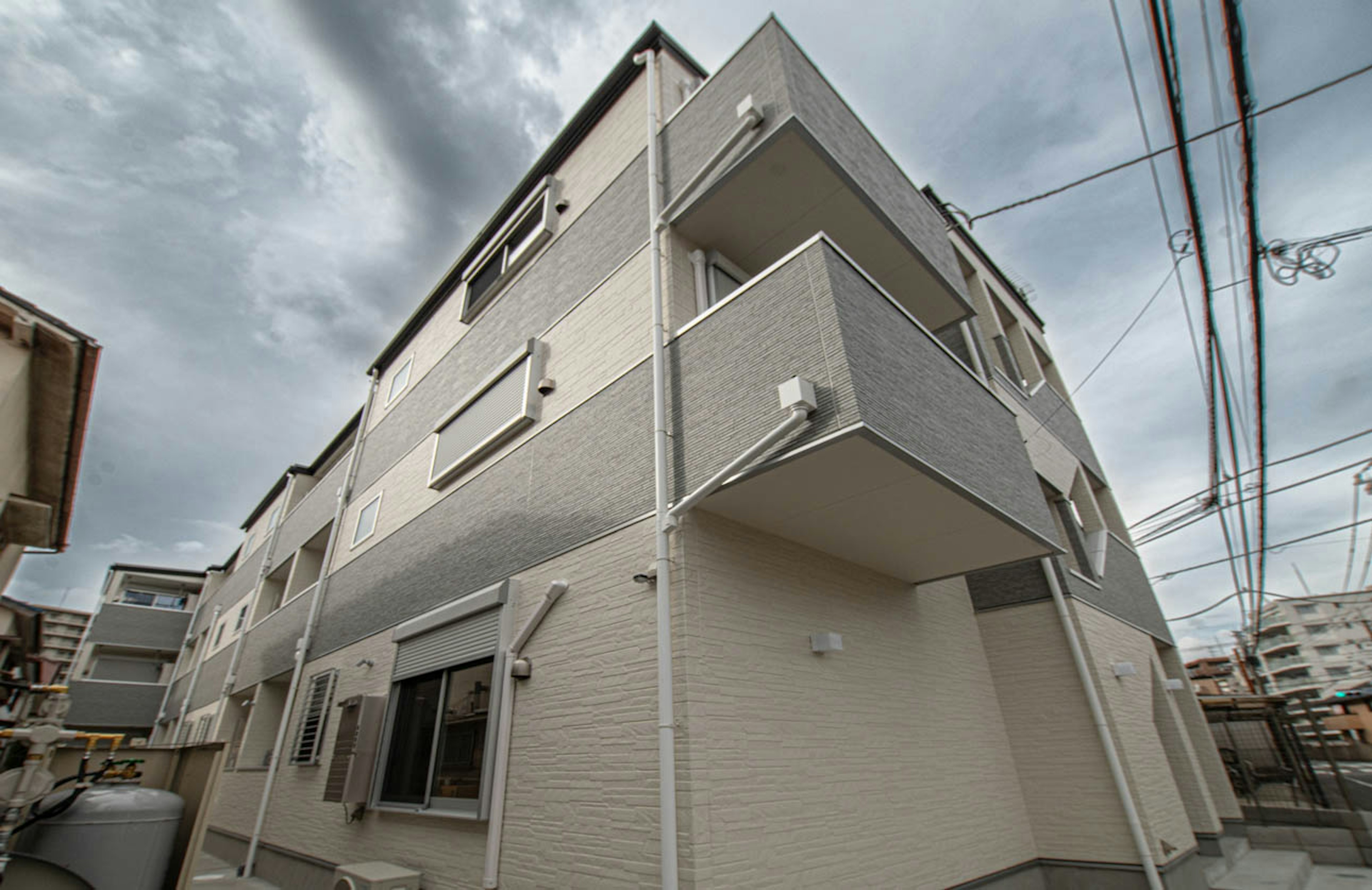 Extérieur d'un appartement de trois étages avec des murs blancs et des balcons sous un ciel nuageux