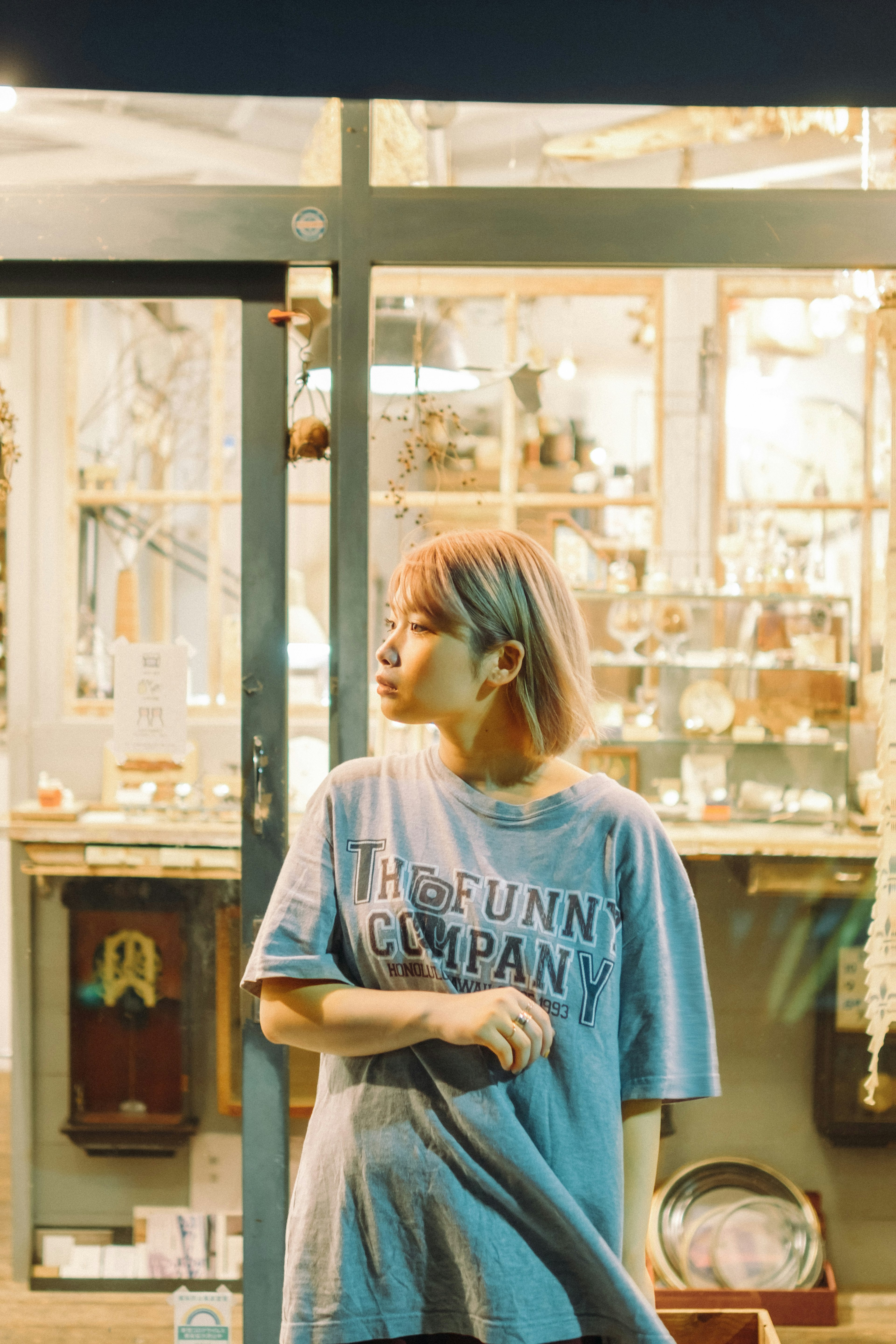 女性が青いTシャツを着て店の前に立っている夜のシーン