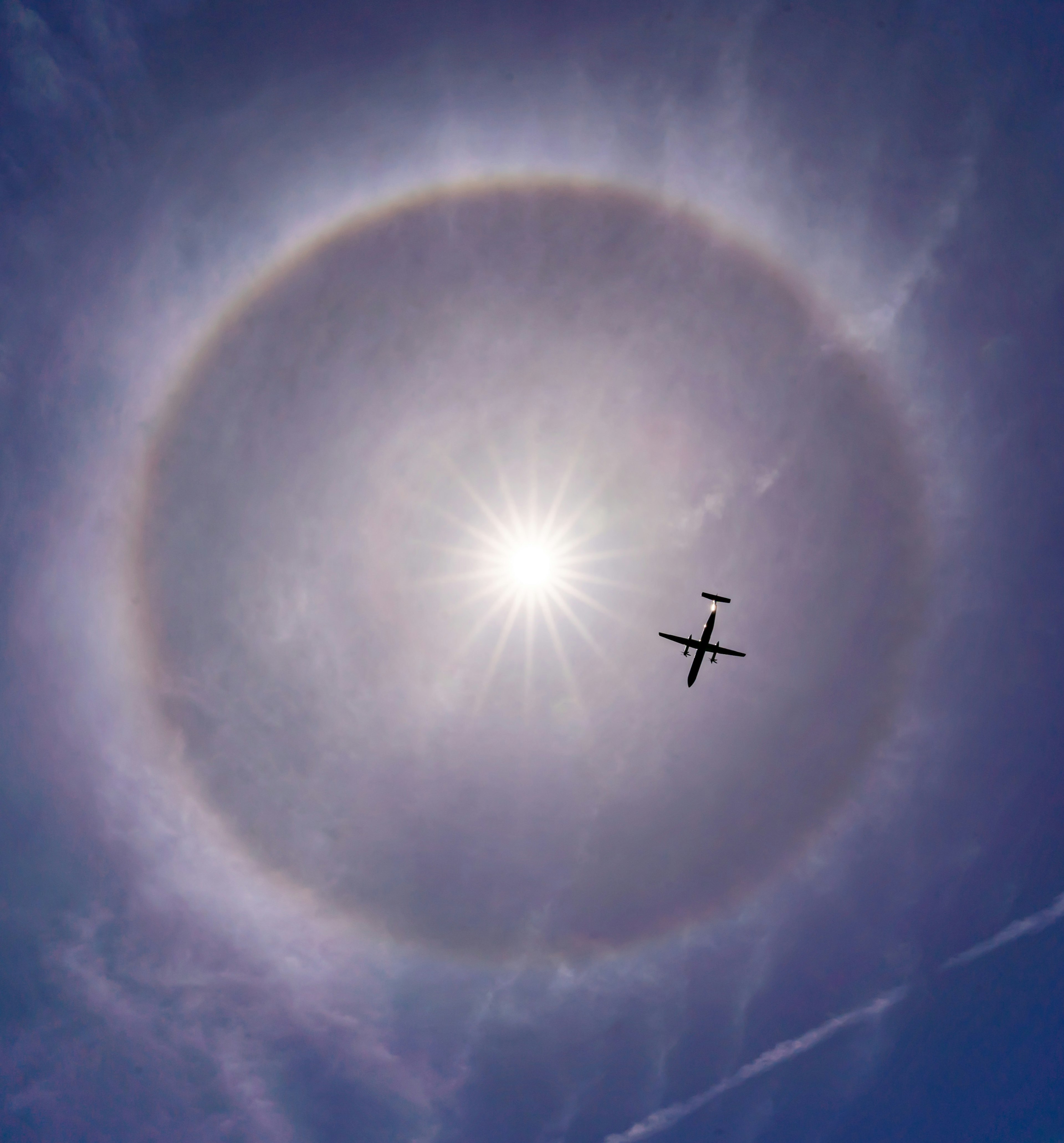 太陽の周りに大きなハロと飛行機が映る青空の写真